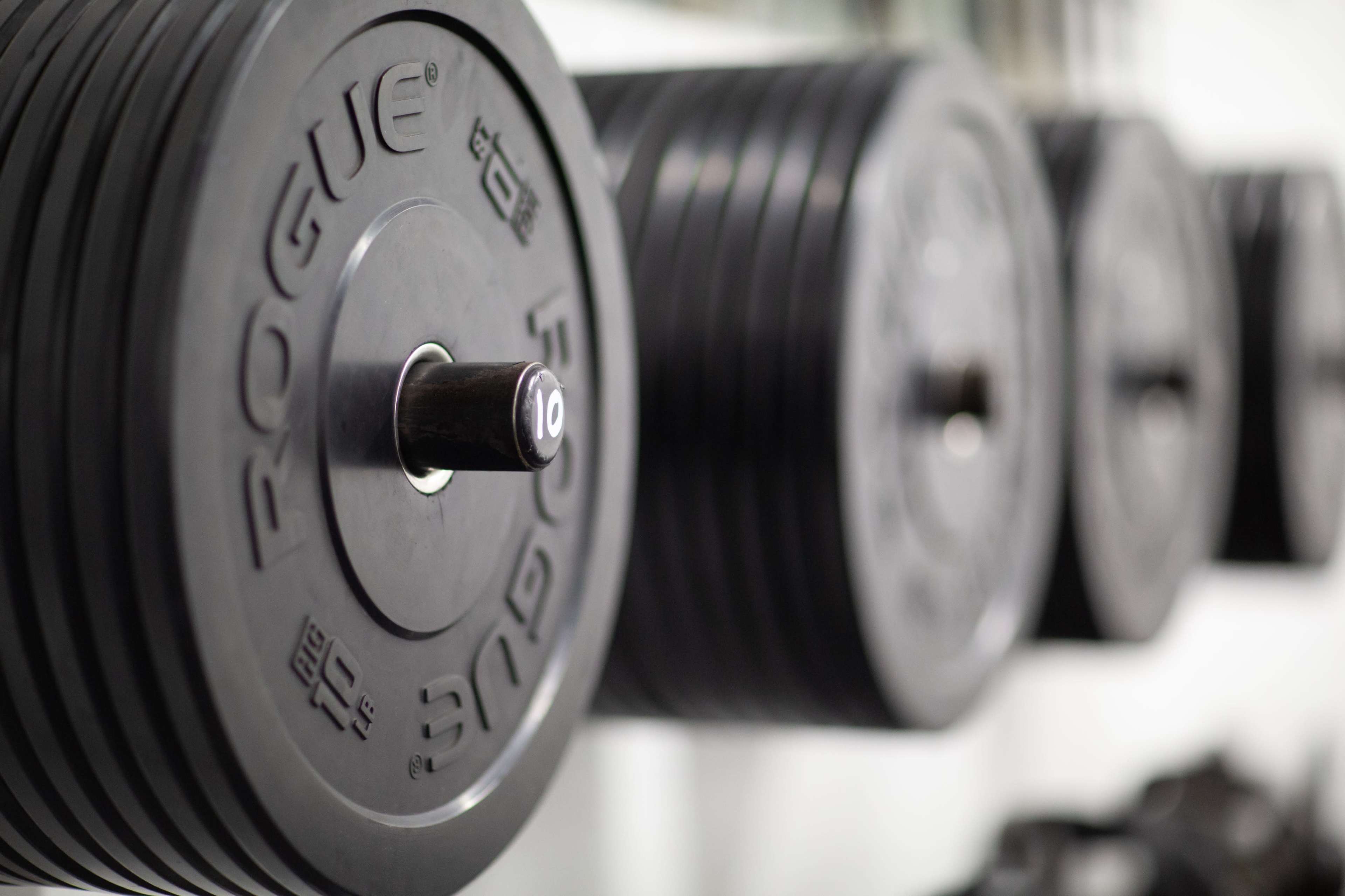 A set of heavy black weight plates is lined up on a rack in a gym.