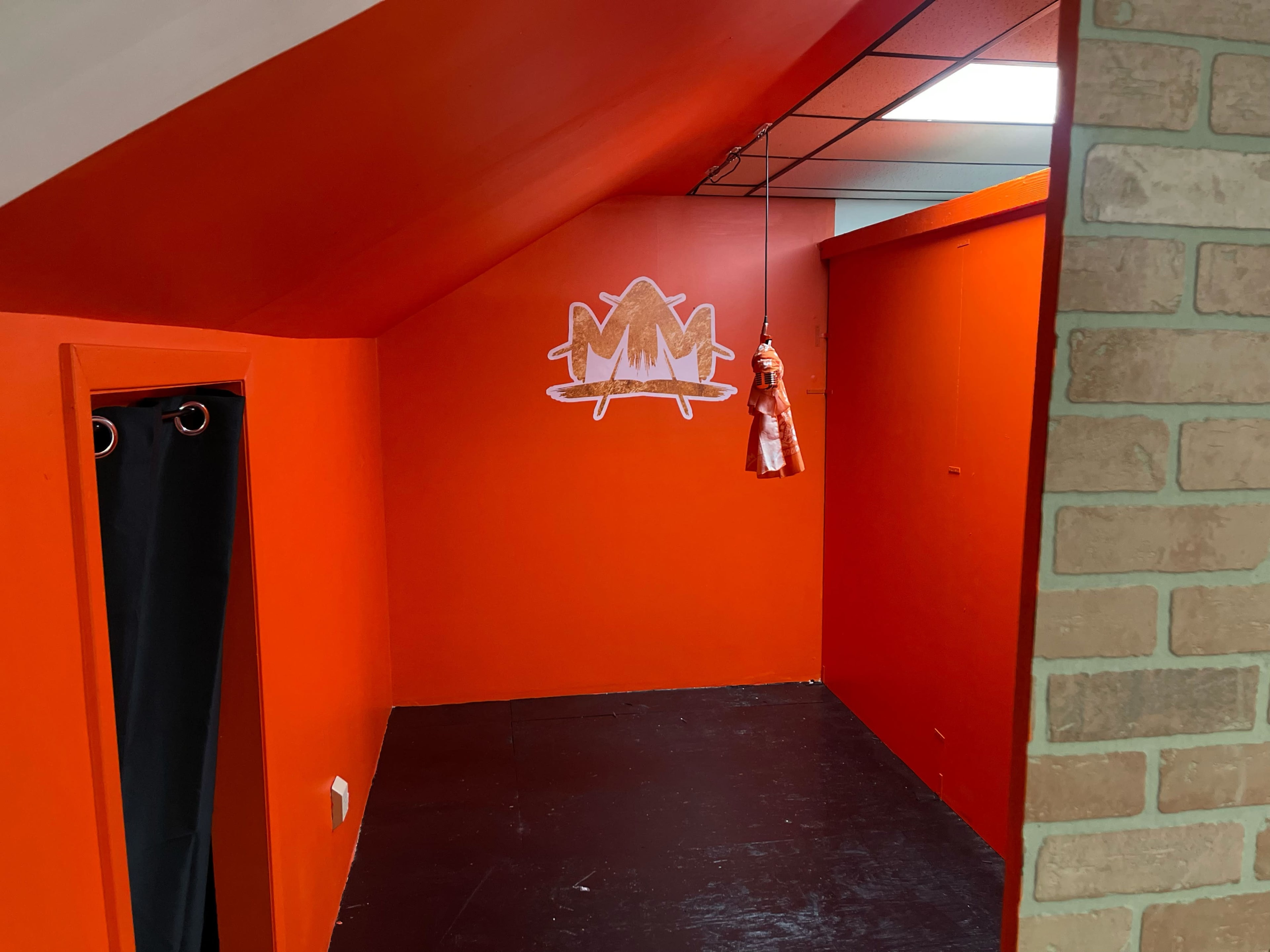A small room with orange walls, a dark floor, and a decorative logo on the back wall.