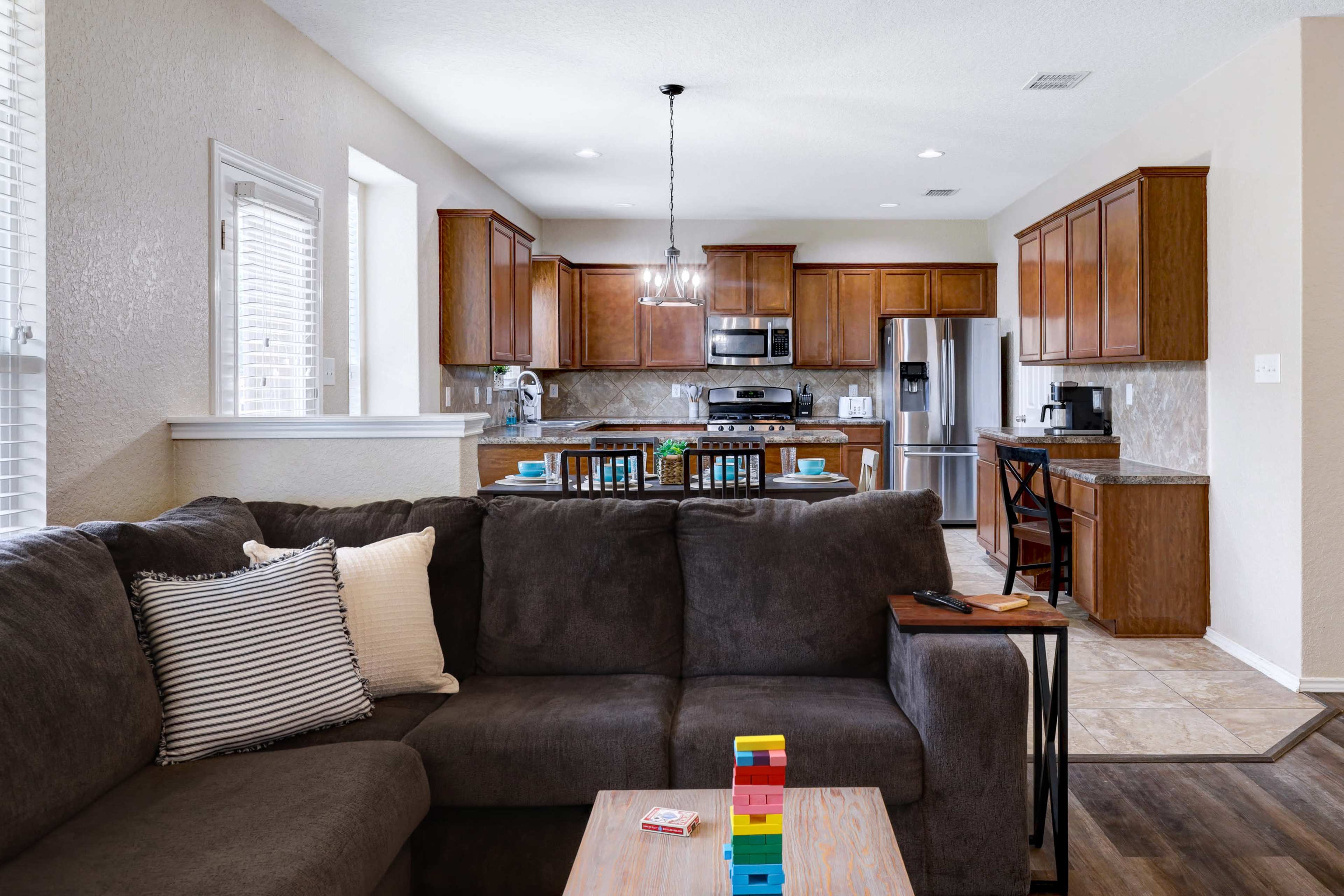 A living room with a dark sofa and a coffee table, overlooking a kitchen with wooden cabinets and stainless steel appliances.