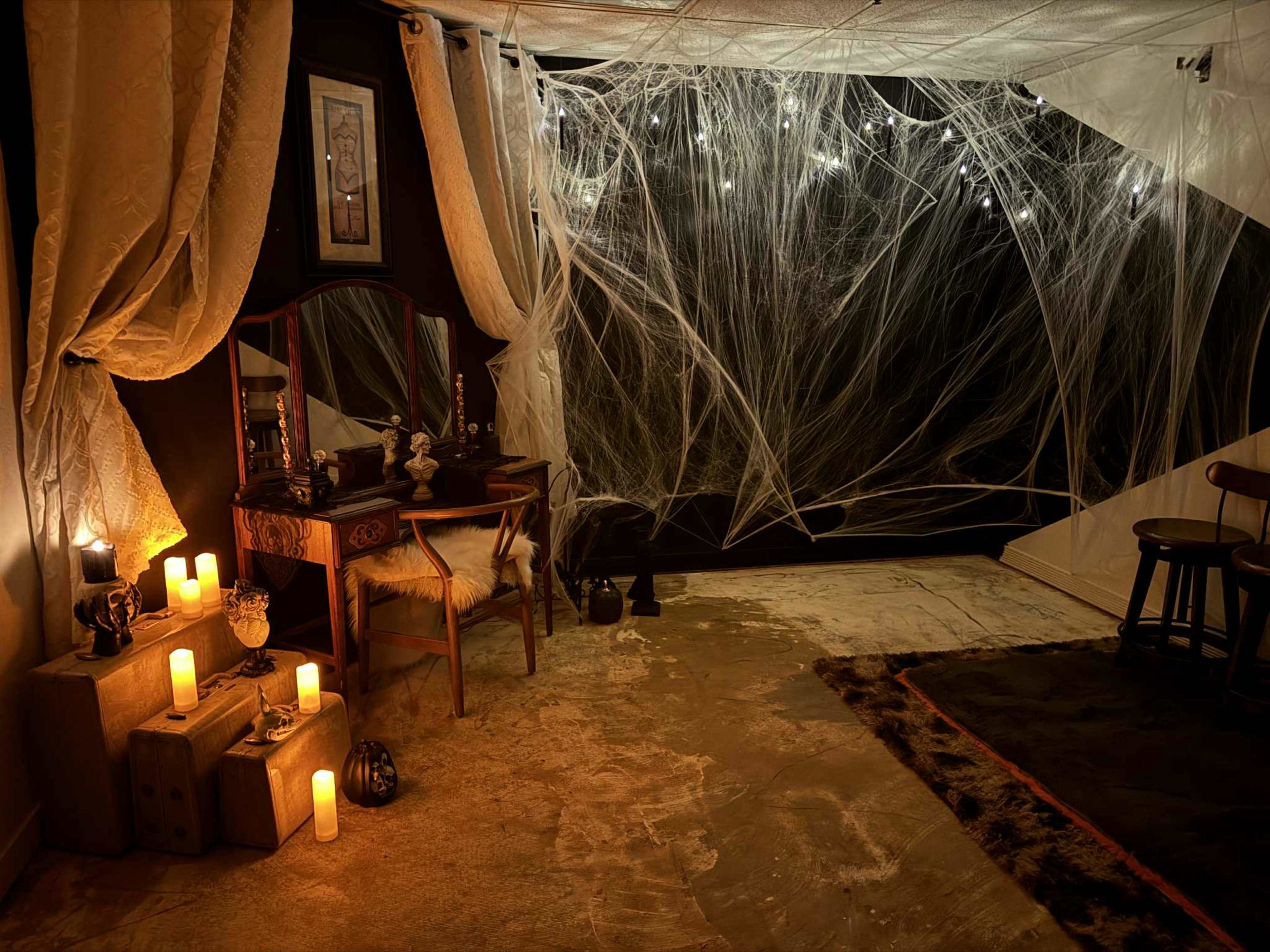 The scene features a dimly lit room adorned with draped fabric, candles, and cobweb-like decorations, creating an eerie atmosphere.