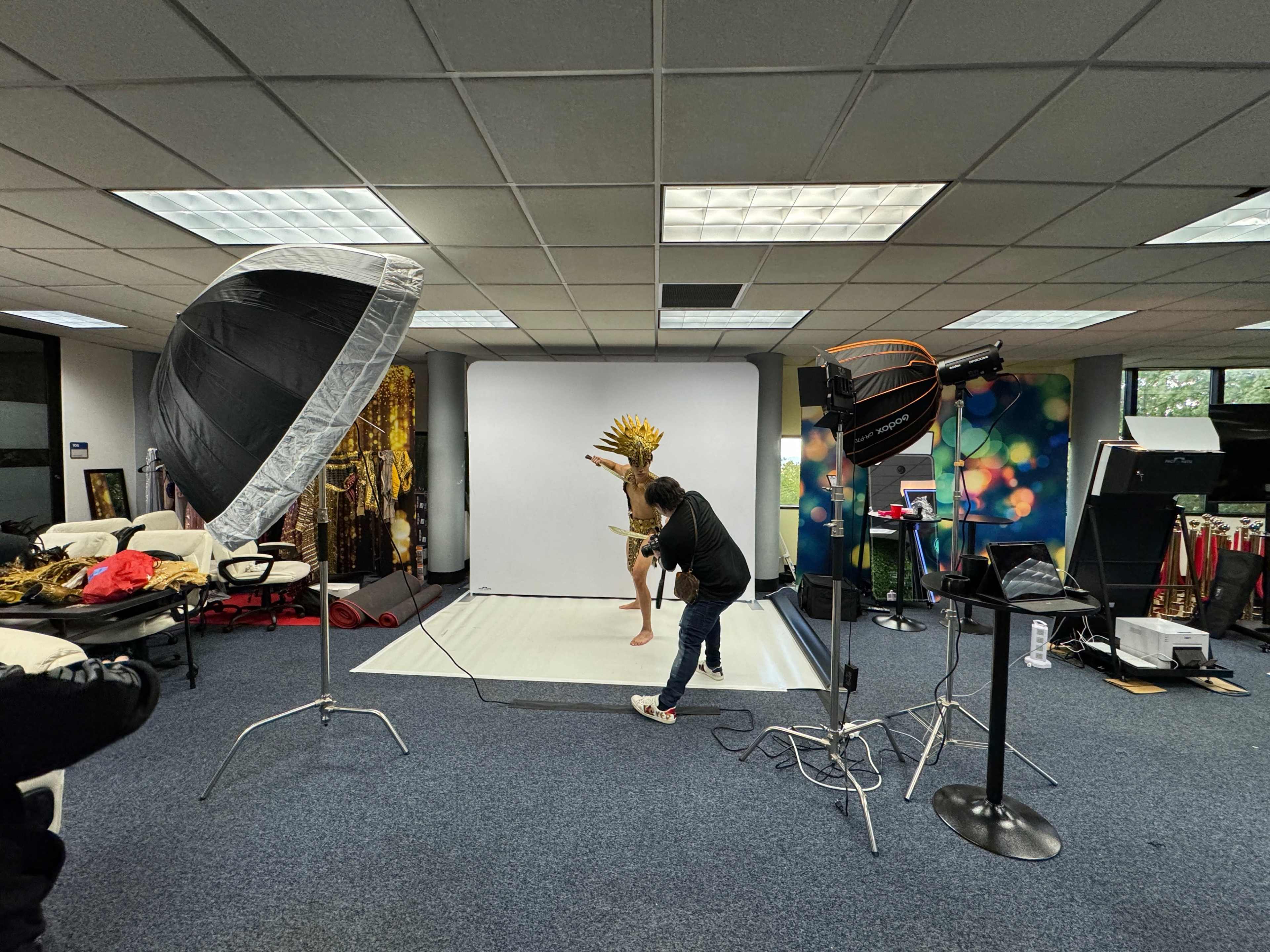 A photographer captures an image of a model posing with a headdress in a studio setting equipped with multiple lighting setups.