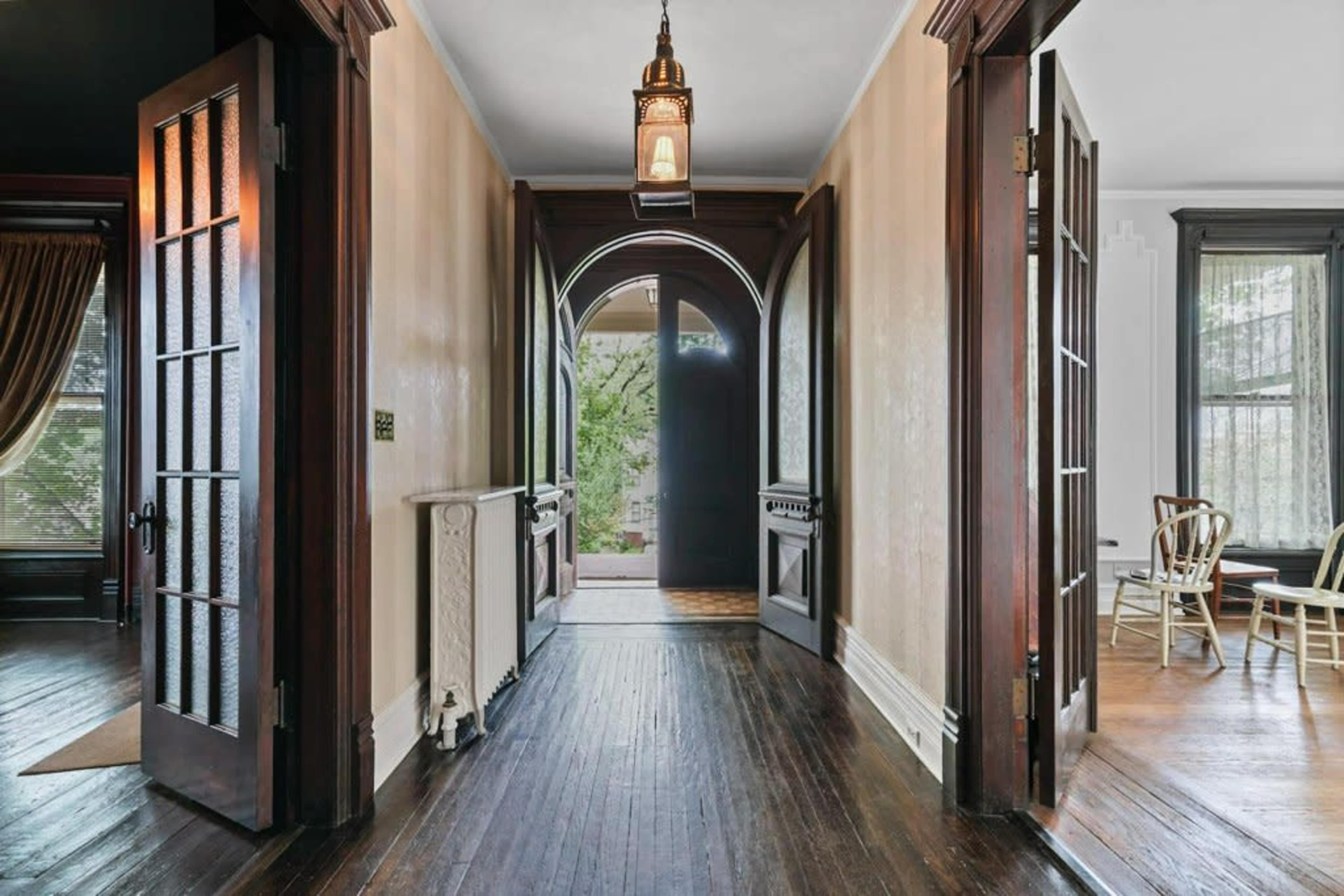 A hallway with arched doorways and wooden floors, featuring doorways leading to adjacent rooms and a lantern hanging from the ceiling.