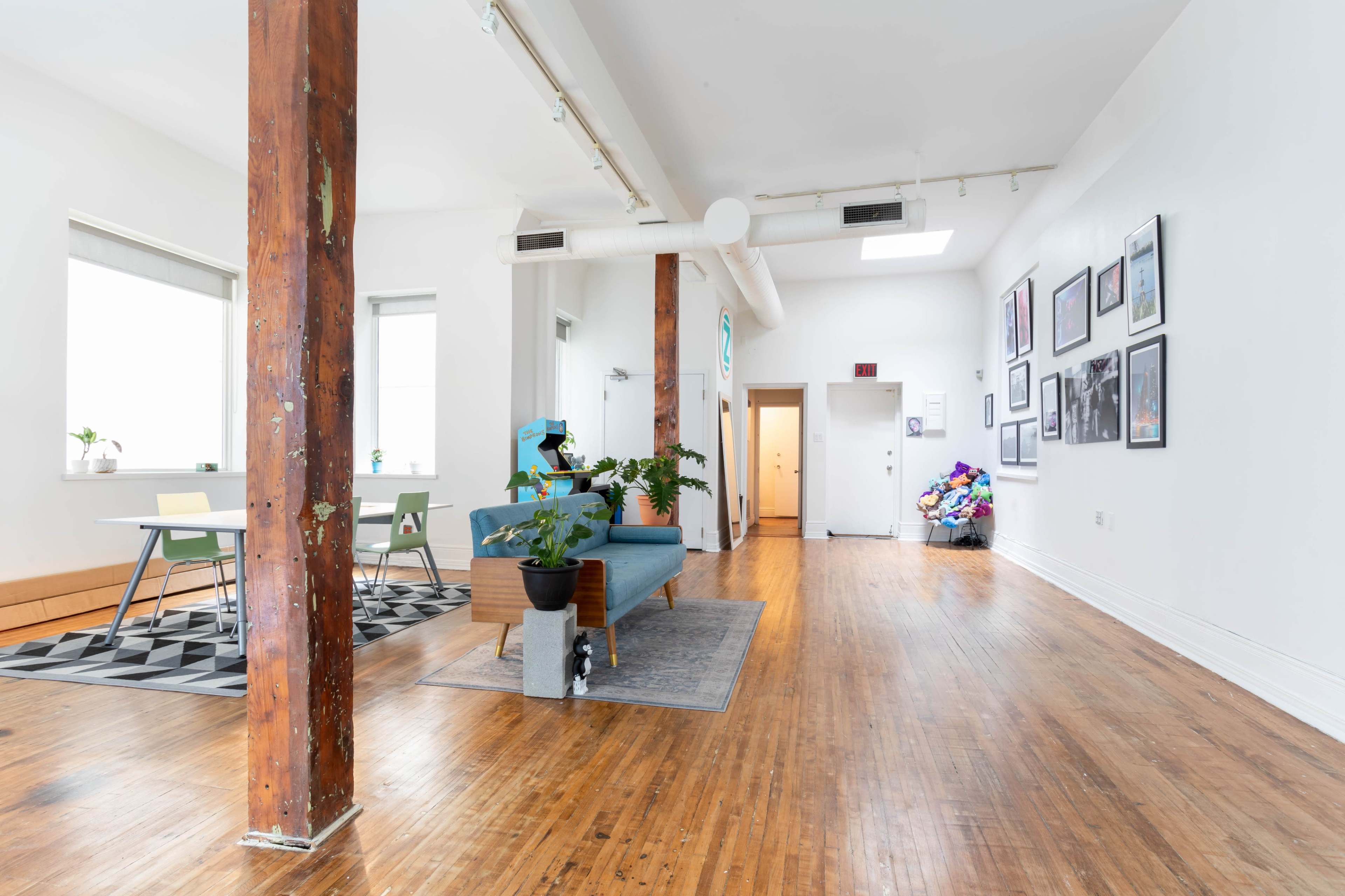 A spacious, well-lit interior featuring wooden floors, a blue couch, a dining table with chairs, and framed artwork on the walls.