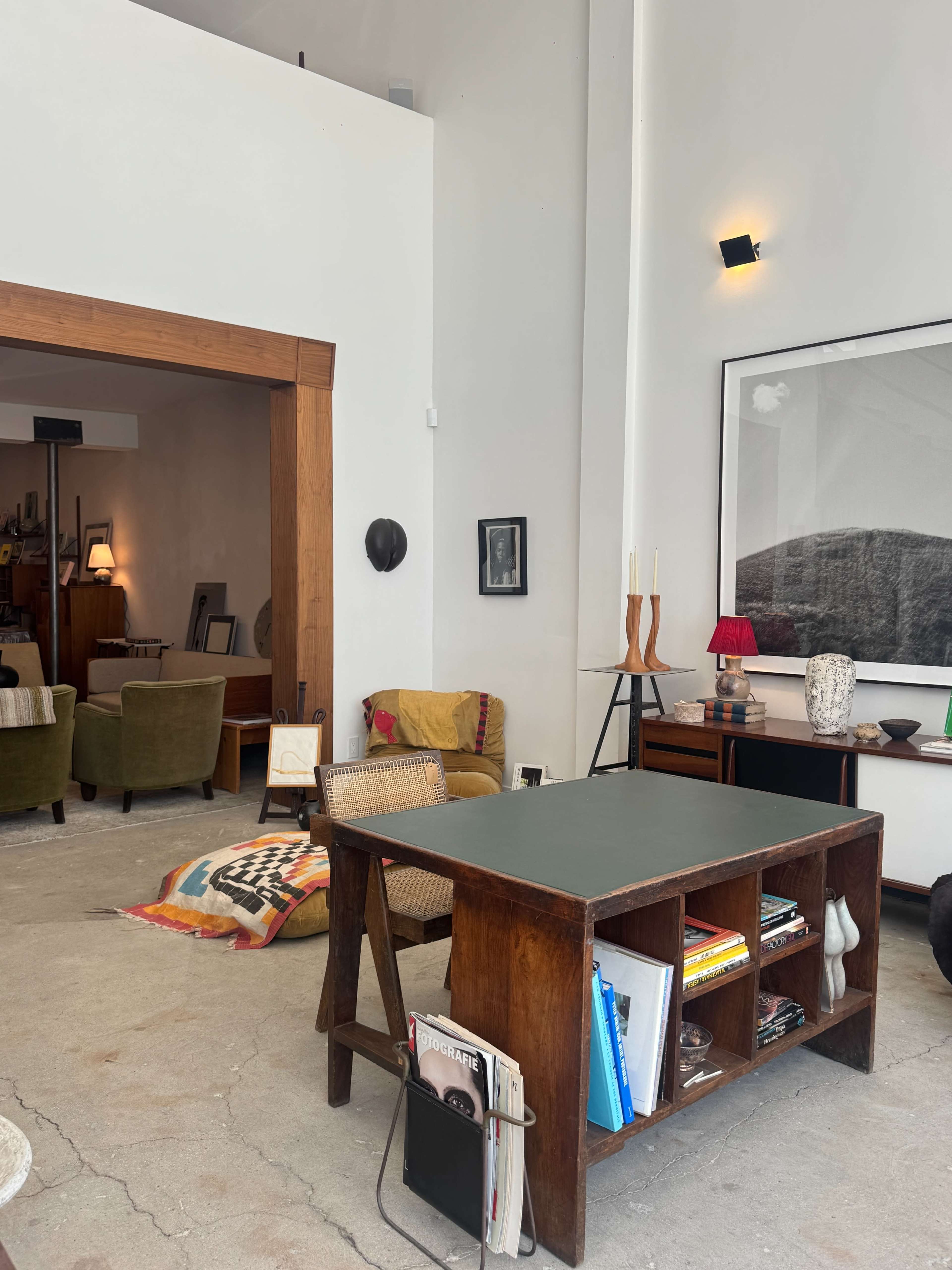 The image shows a modern living space featuring a wooden table with shelves, a cozy seating area in the background, and various decorative items on display.