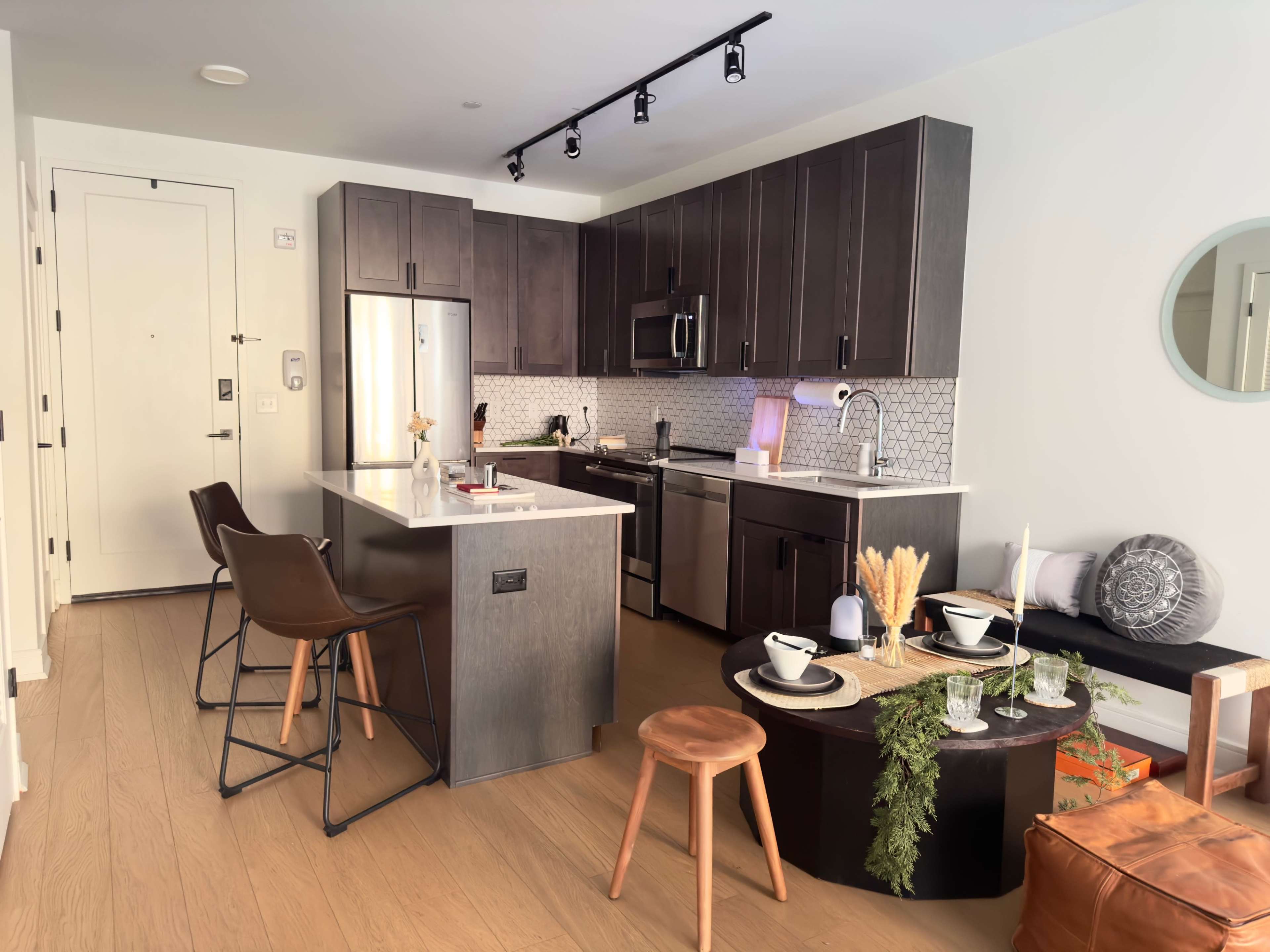 A modern kitchen with dark wood cabinets, stainless steel appliances, a central island with bar stools, and a dining table set with dishware and decorative items.