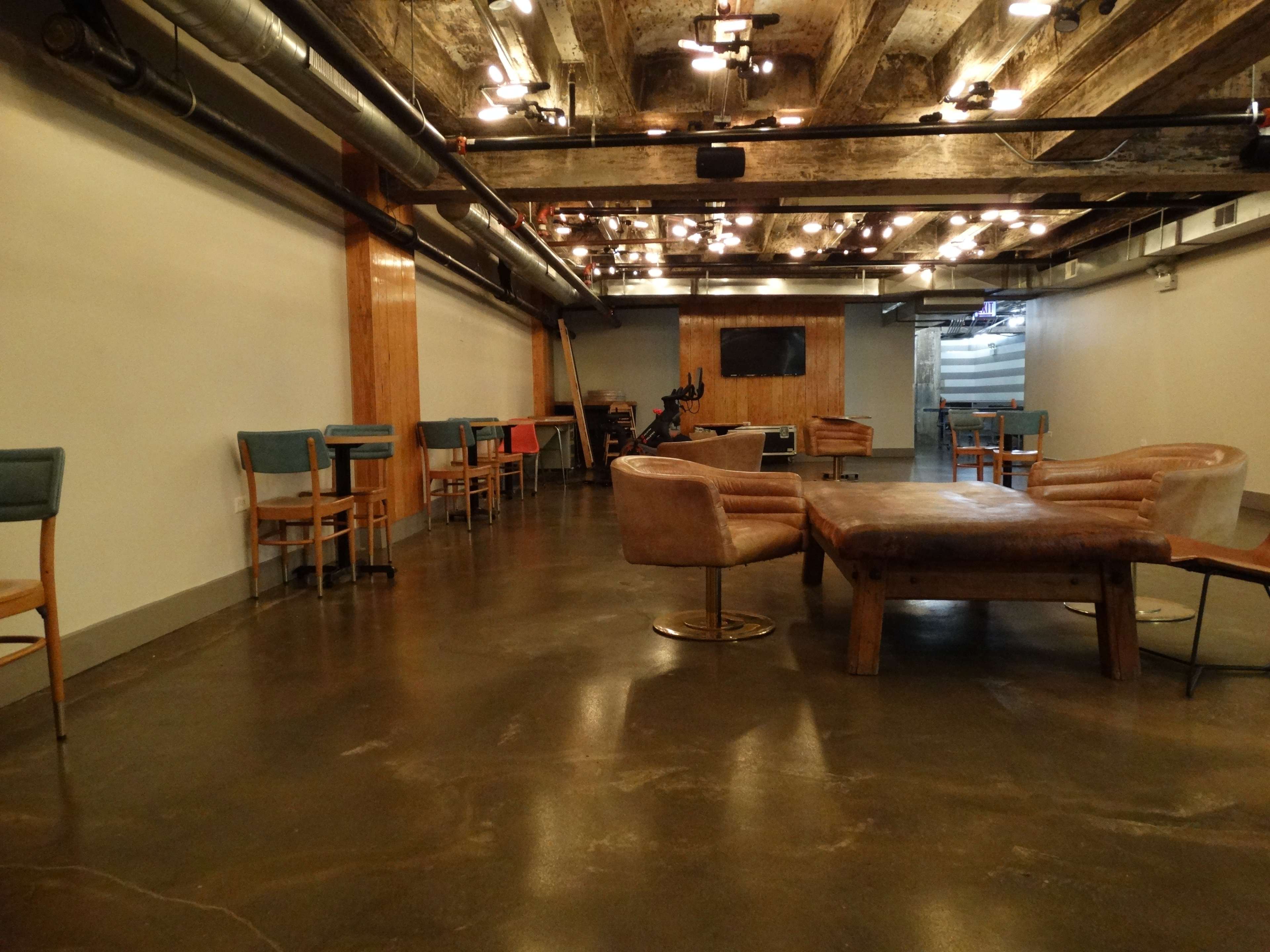 A modern, industrial-style interior with wooden beams and furniture, featuring a spacious area with chairs and a large table.