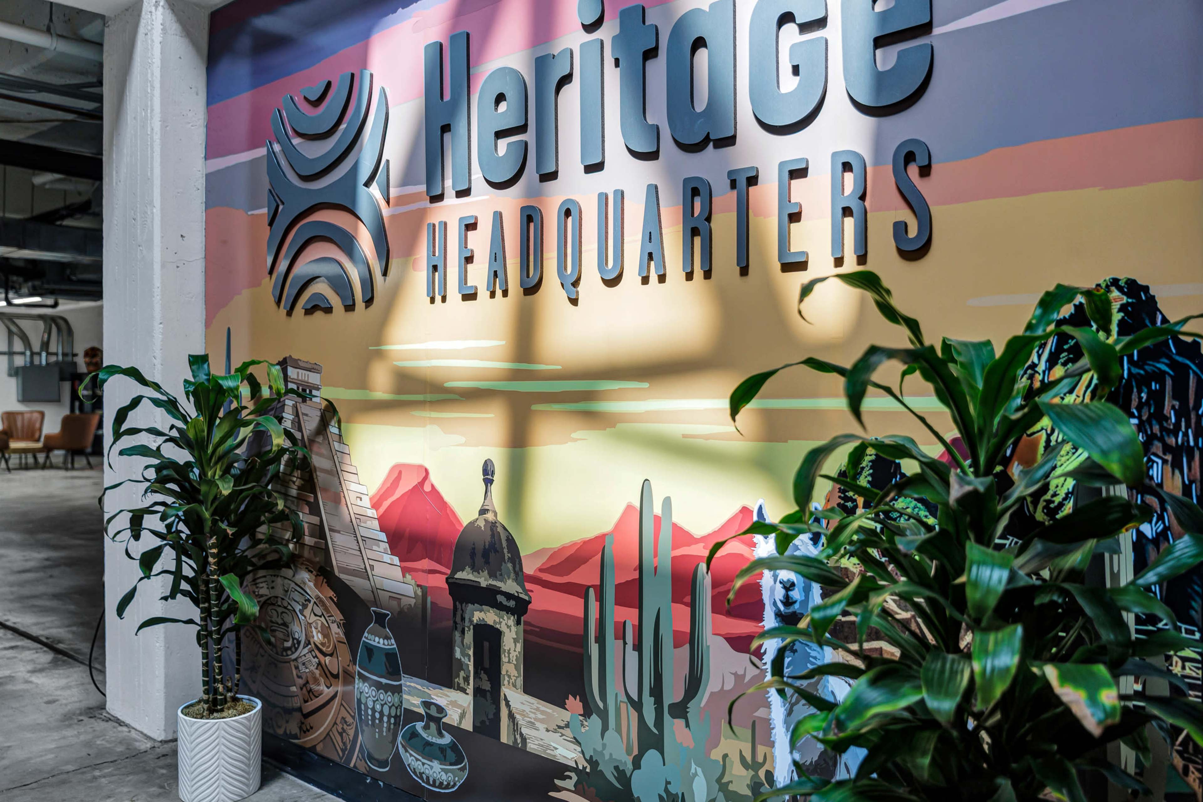The image features a colorful mural with the text "Heritage Headquarters" prominently displayed, accompanied by decorative plants and a backdrop of desert landscapes.