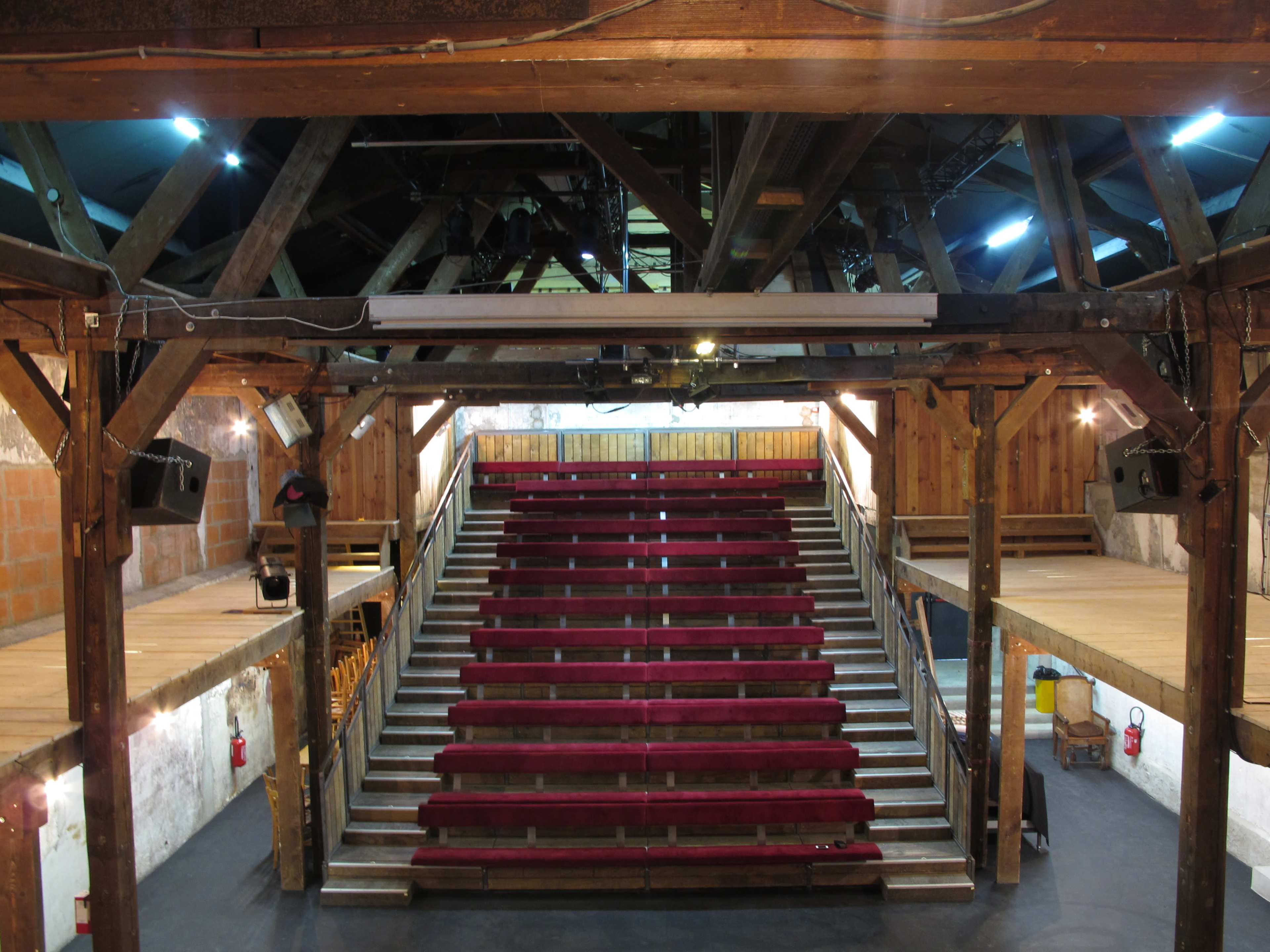 A large, open auditorium with wooden beams and tiered seating arranged in red fabric.