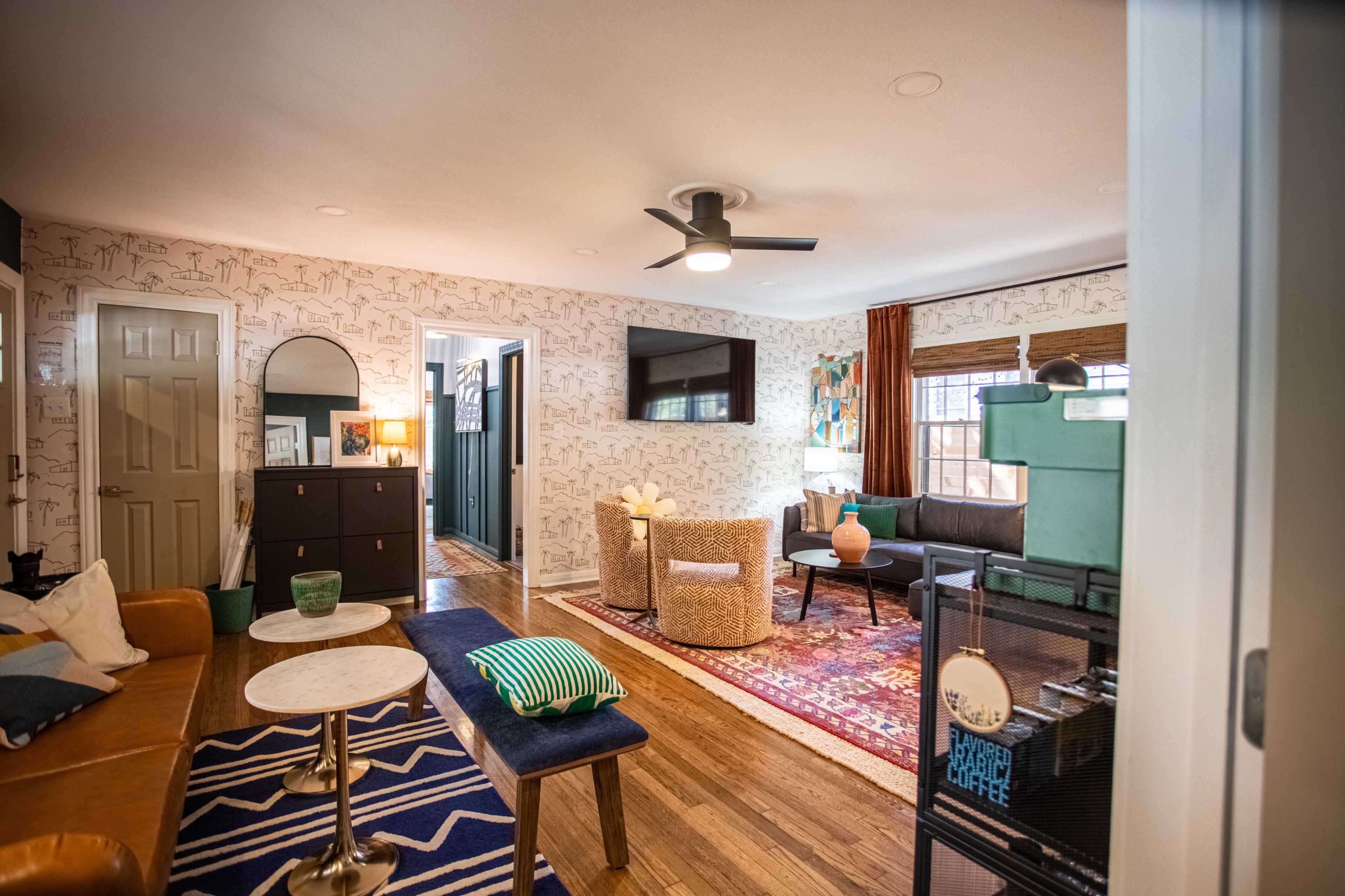 The living area features a mix of modern furniture, a patterned area rug, and decorative wall art.