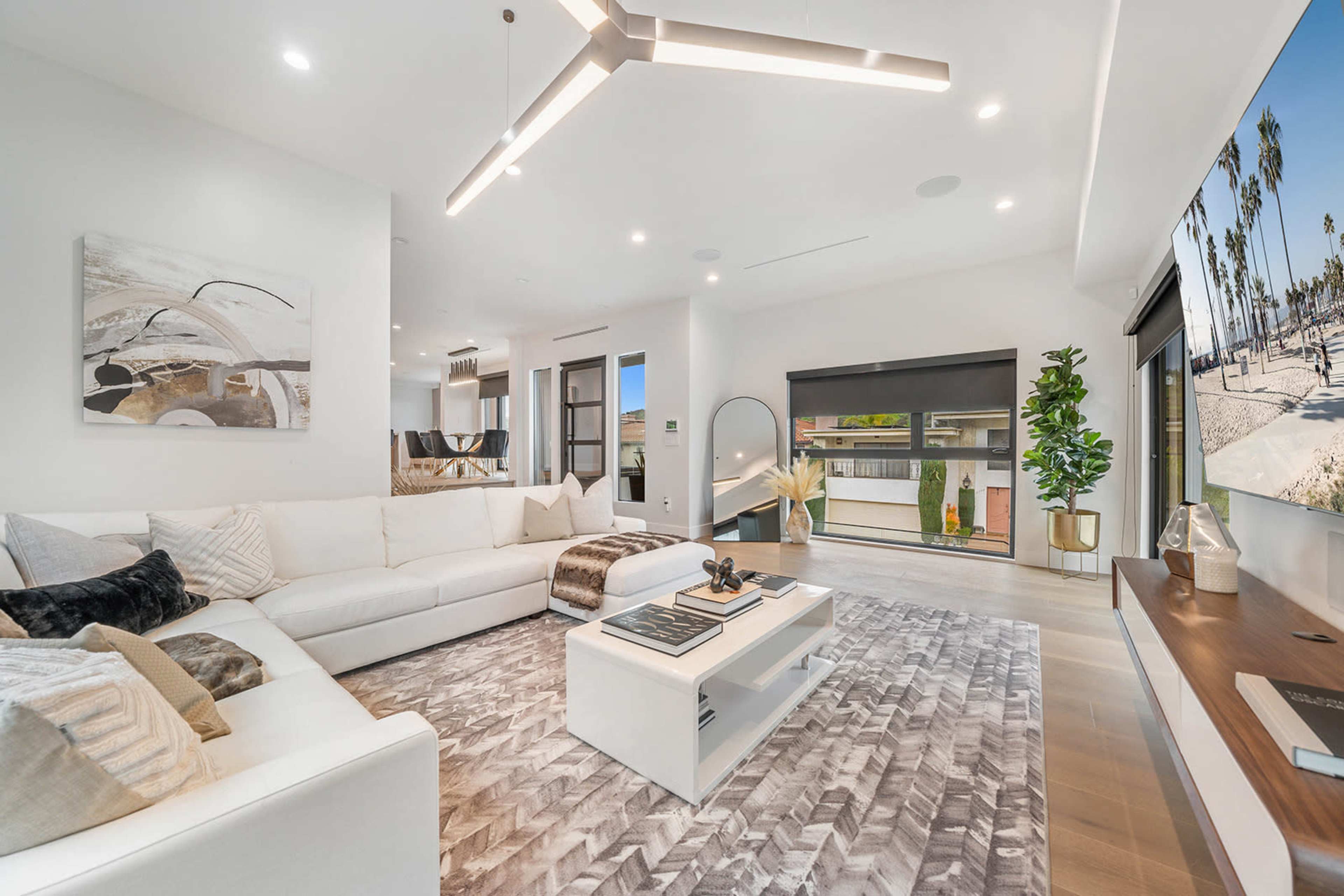 A spacious living room features a large sectional sofa, a modern coffee table, and a wall-mounted television, with sliding glass doors leading to an outdoor area.