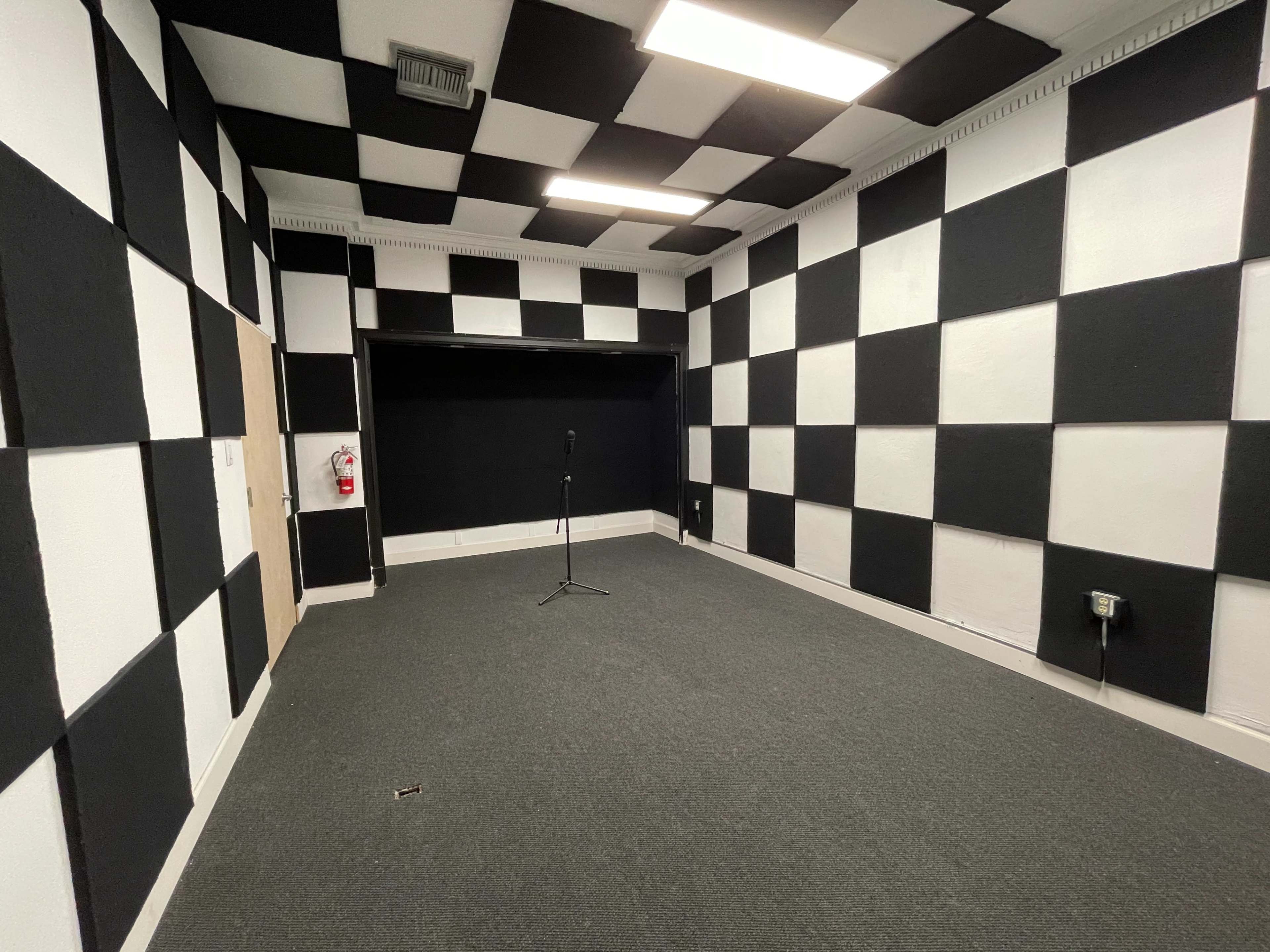 A room with black and white checkered walls, a gray carpet, and a microphone stand in the center.