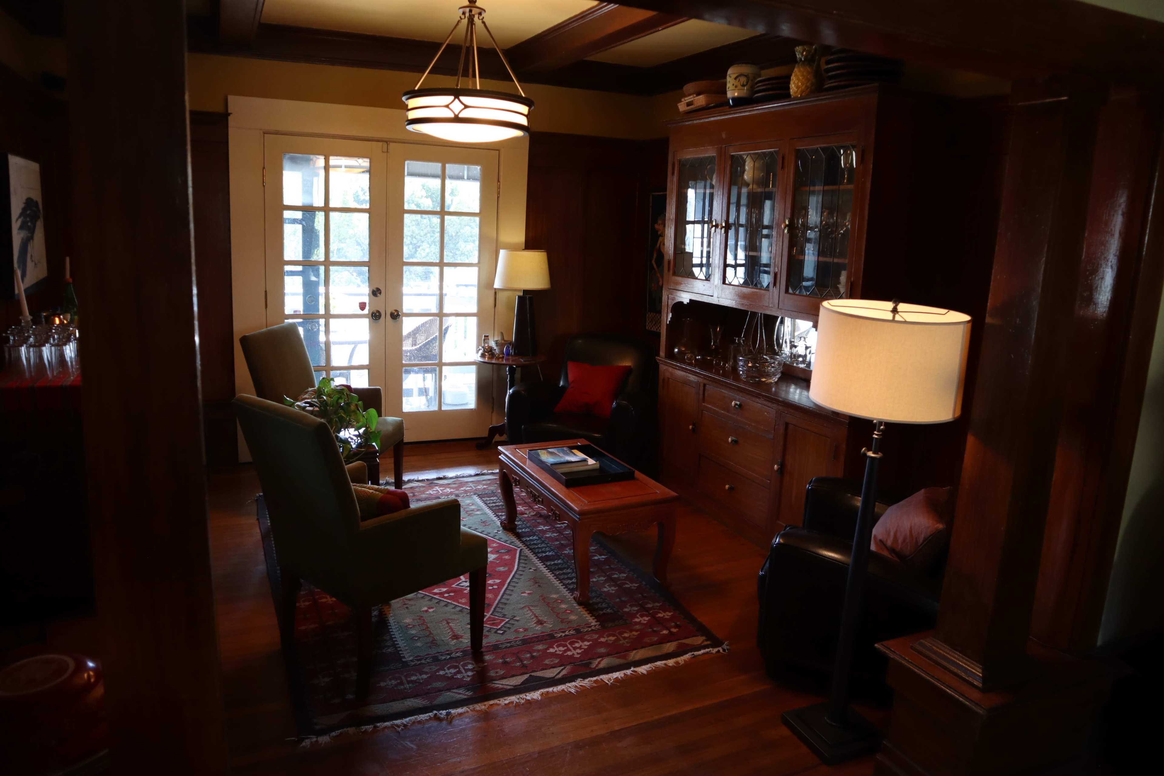 The image shows a cozy living room with two chairs, a coffee table, and a side table next to a lamp, featuring wooden furniture and glass doors leading outside.