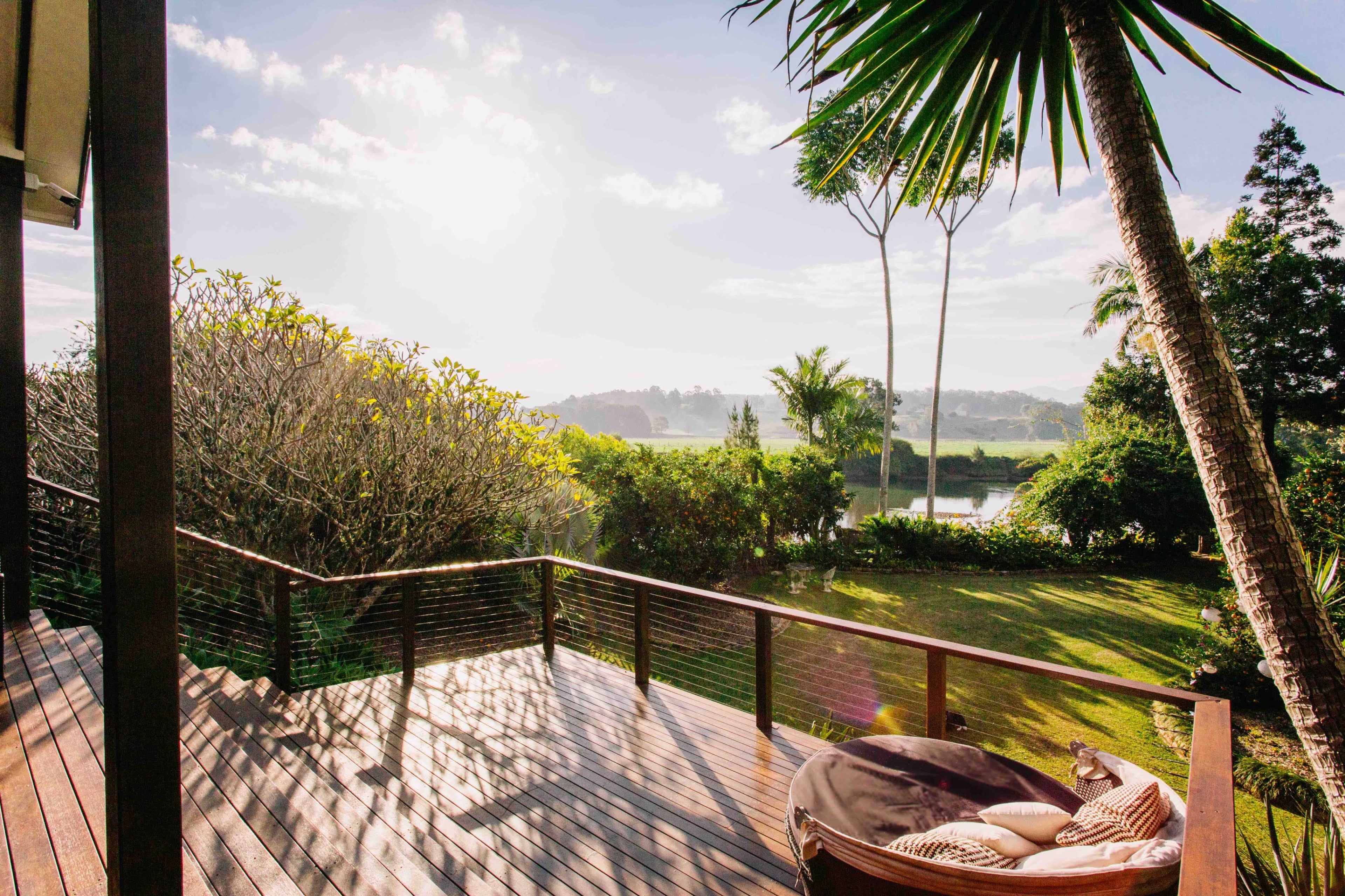 A wooden deck overlooks a lush green landscape with trees and a sunlit sky in the background.