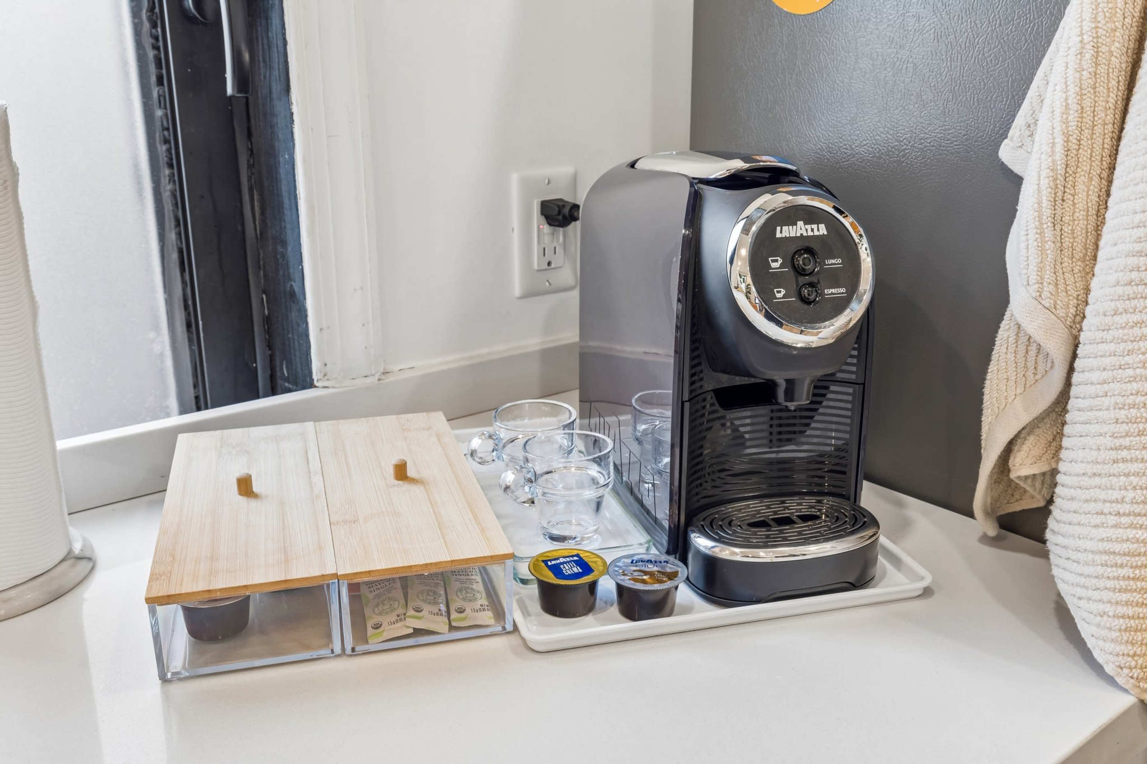 A countertop coffee maker is set up beside a cutting board and several glass cups on a tray.