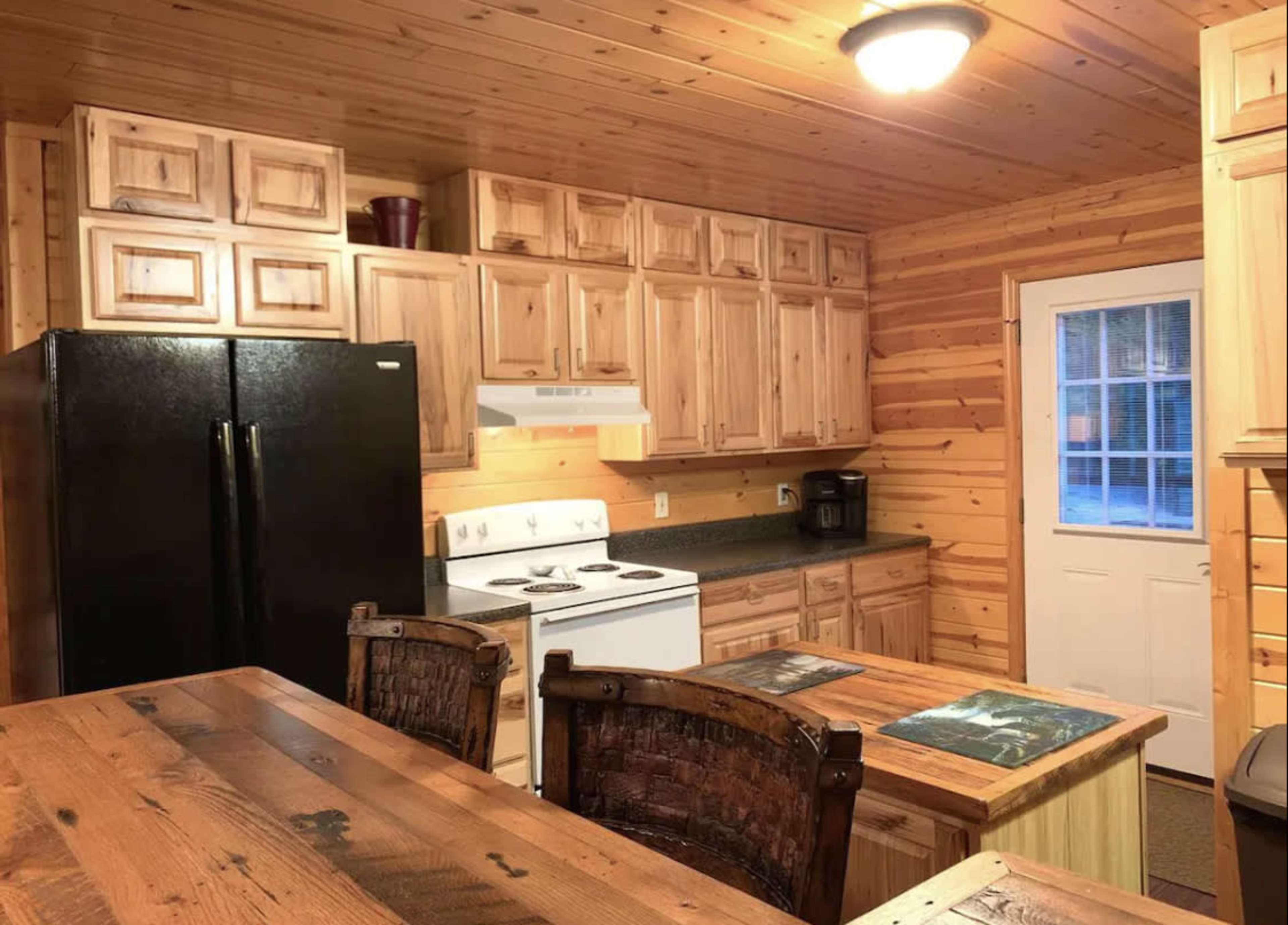A wooden cabin kitchen with a black refrigerator, white stove, and a wooden dining table surrounded by chairs.