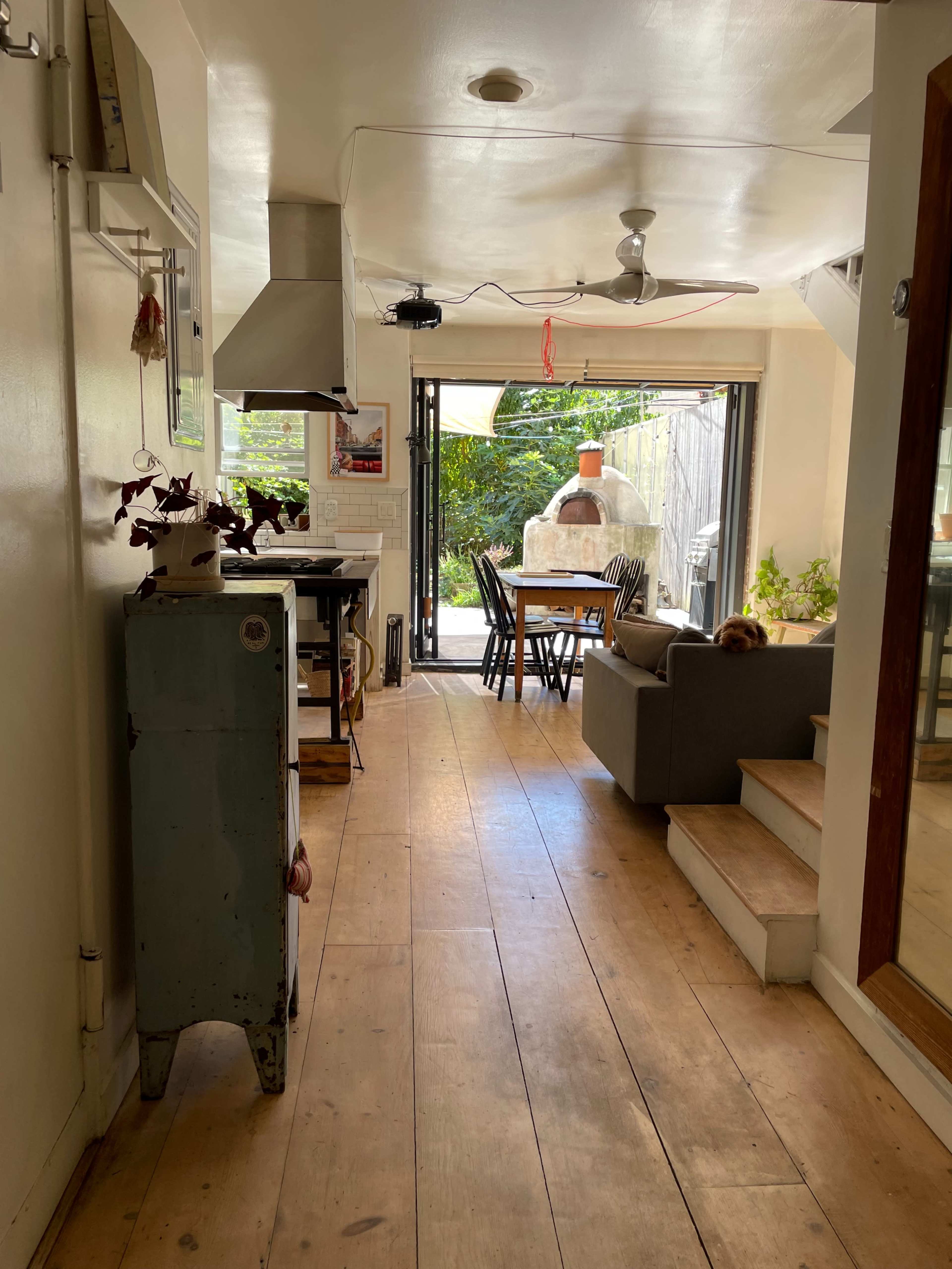A narrow hallway leads to an open dining area with a table and chairs, featuring a large window that opens to an outdoor space.