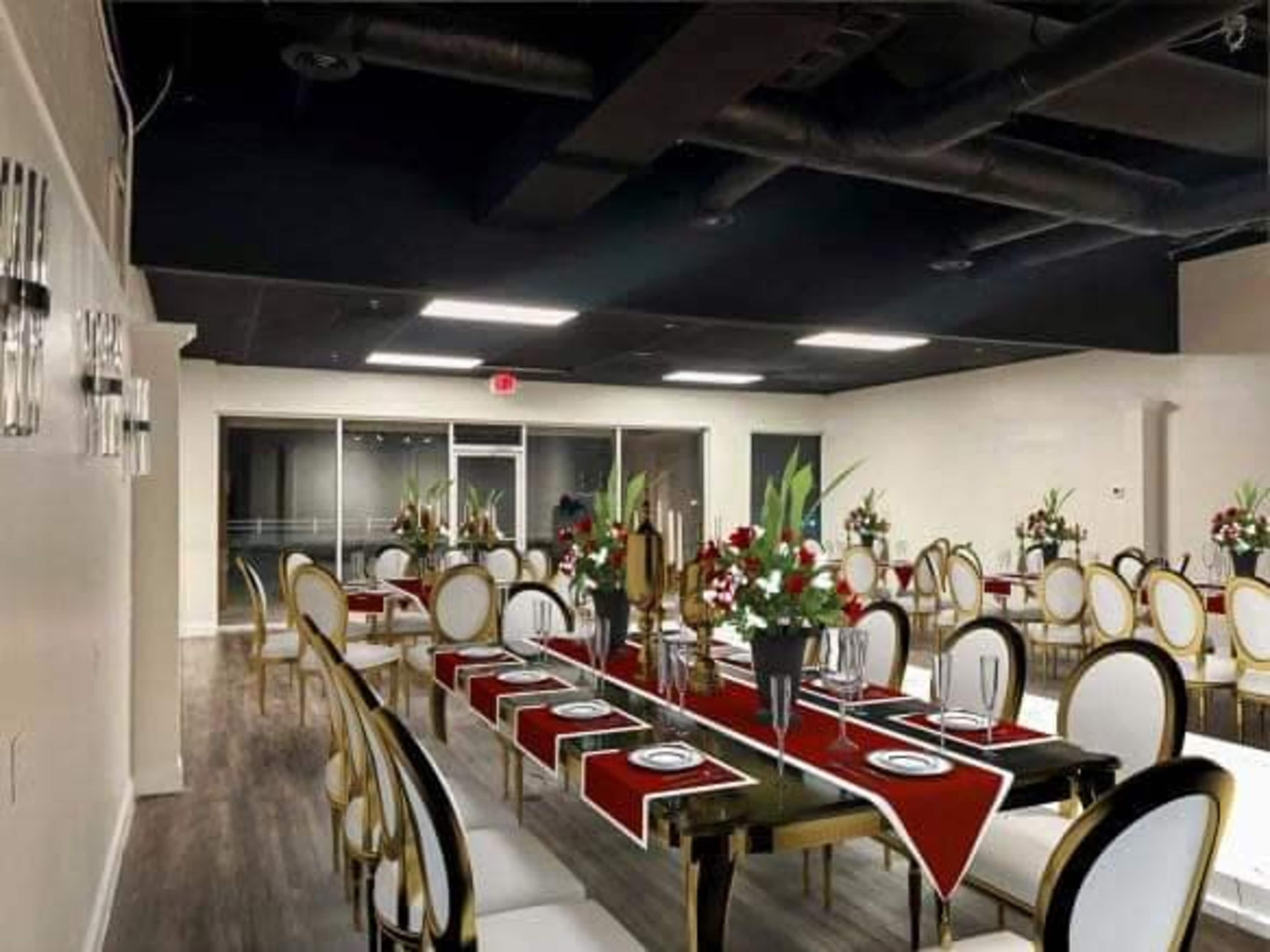 A spacious dining area features elegantly set tables with red runners and floral centerpieces, designed for events.
