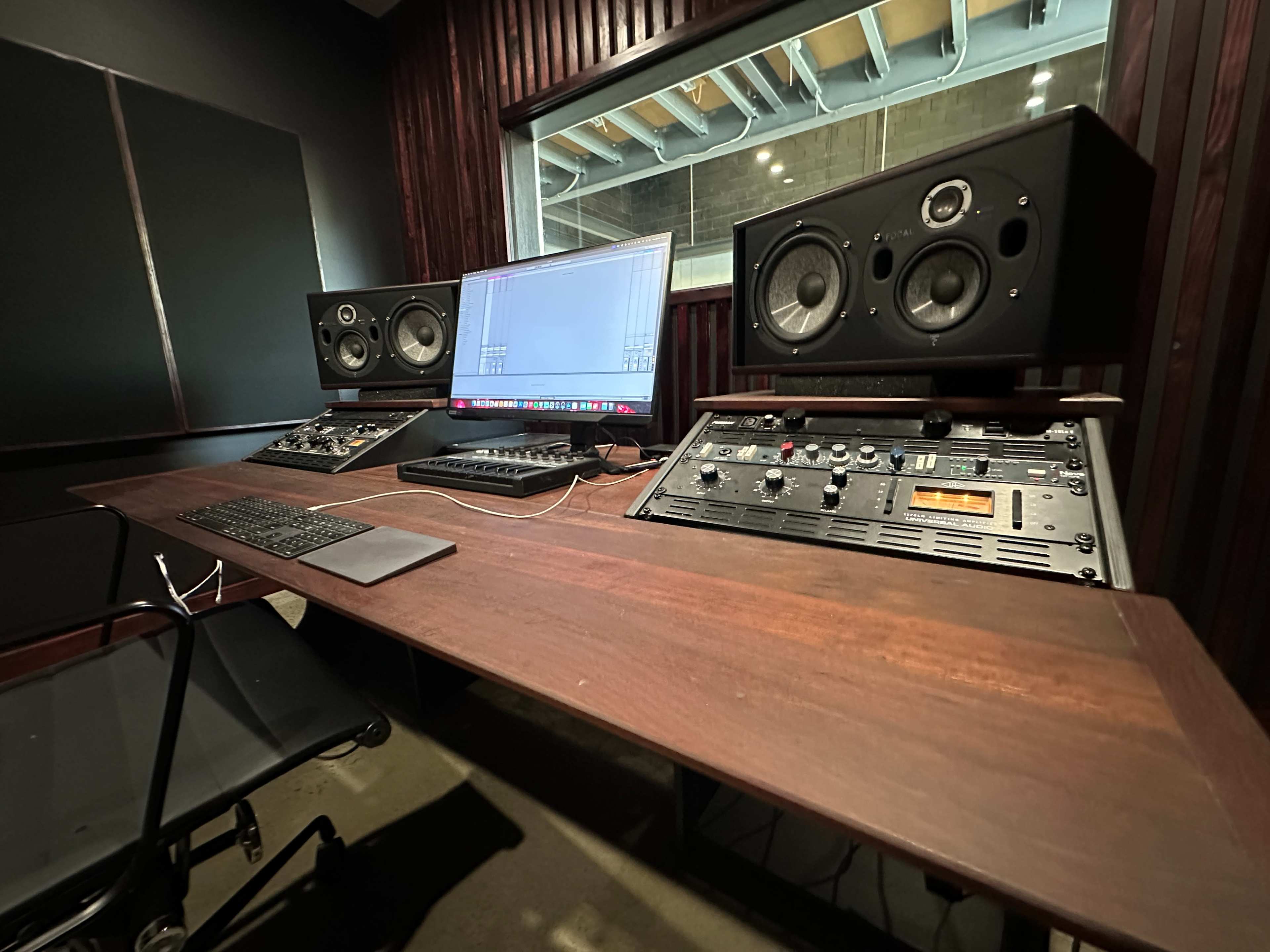 A professional audio mixing studio with a computer, mixing console, and two large speakers positioned on a wooden desk.
