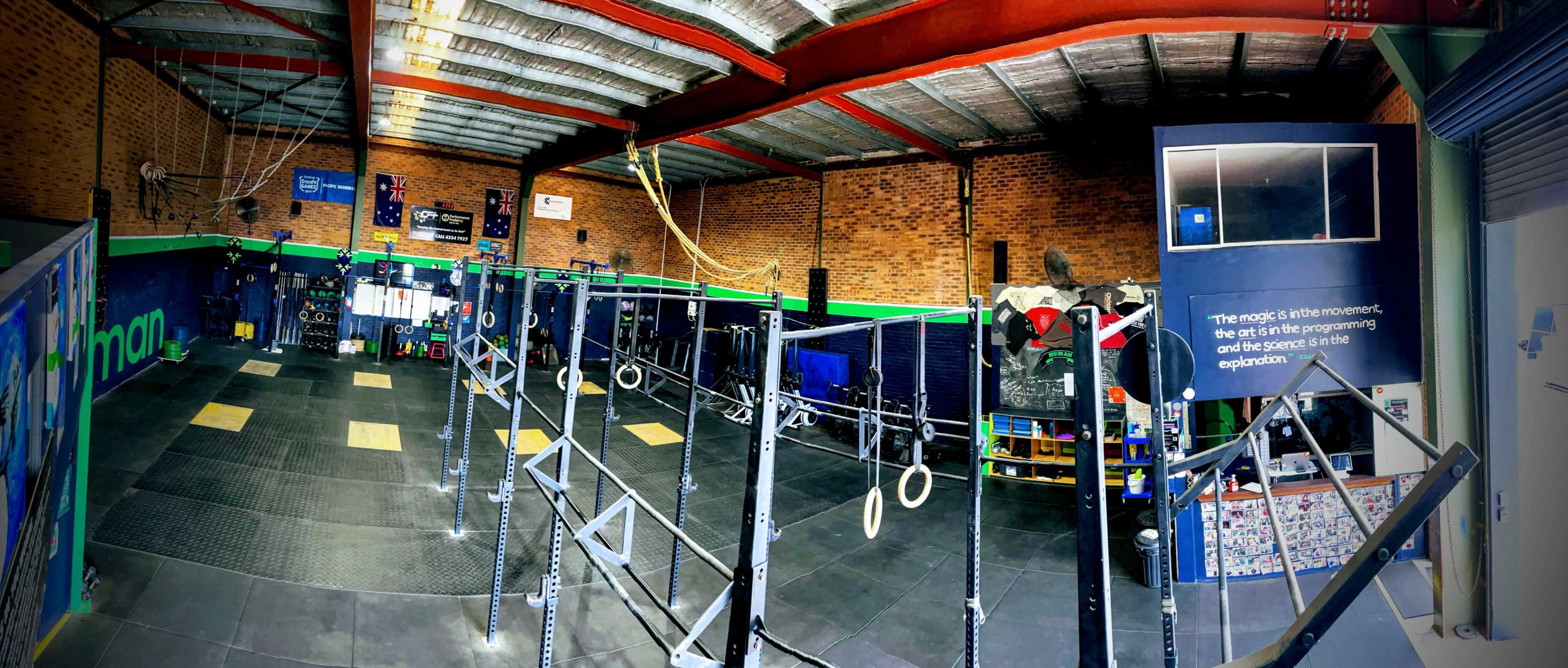A spacious gym with various workout equipment, including a set of rings, pull-up bars, and fitness mats, in a well-lit, brick-finished environment.