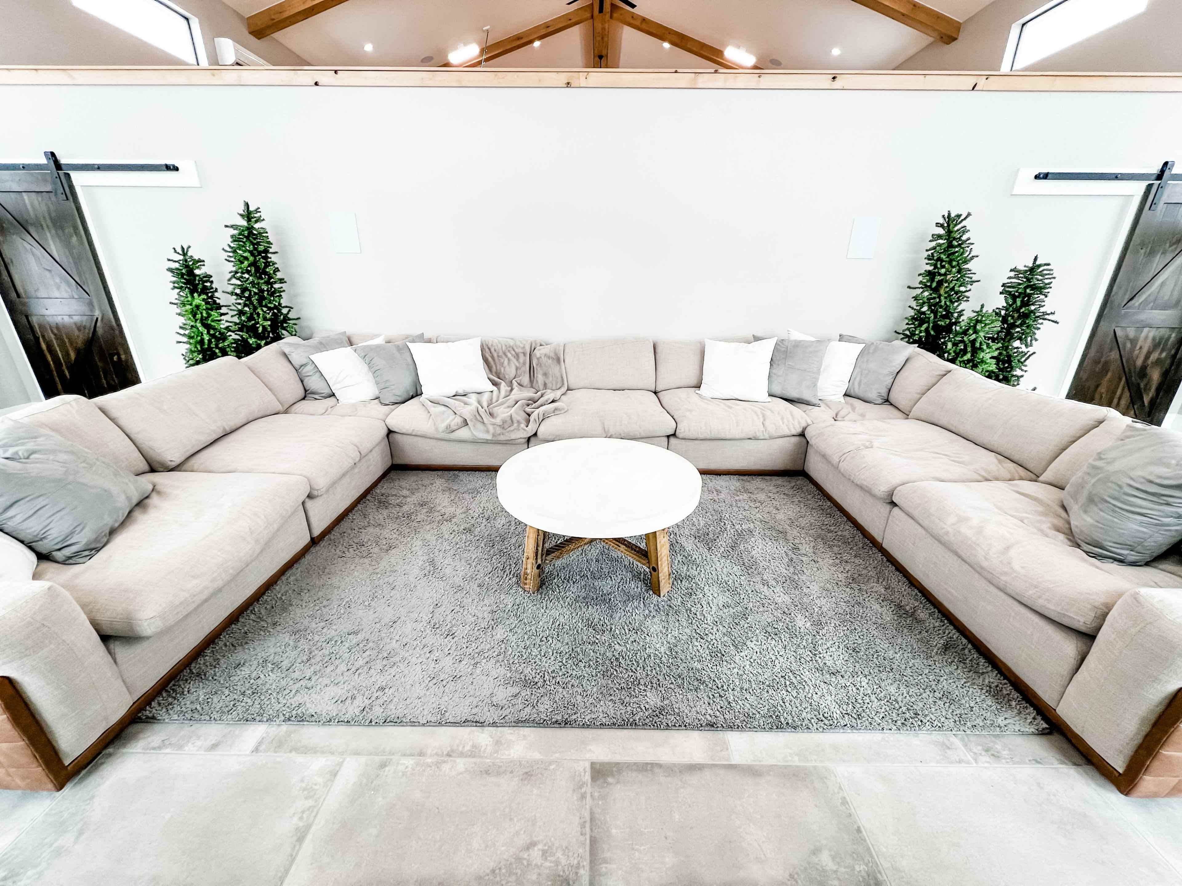 A spacious living area with a large L-shaped beige sectional sofa surrounding a round white coffee table on a gray rug.