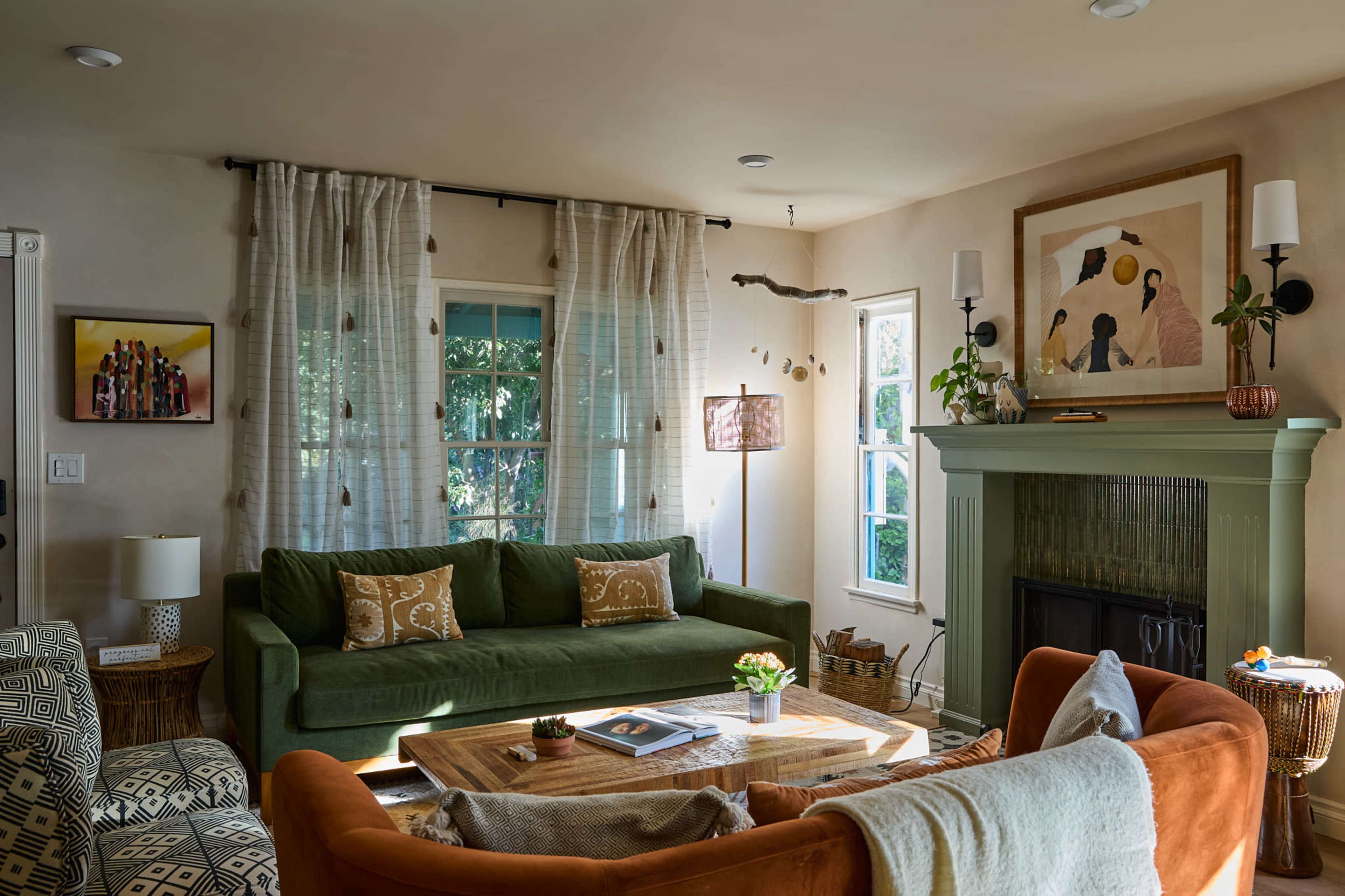 The living room features a green sofa, a brown armchair, a wooden coffee table, and large windows adorned with light curtains.