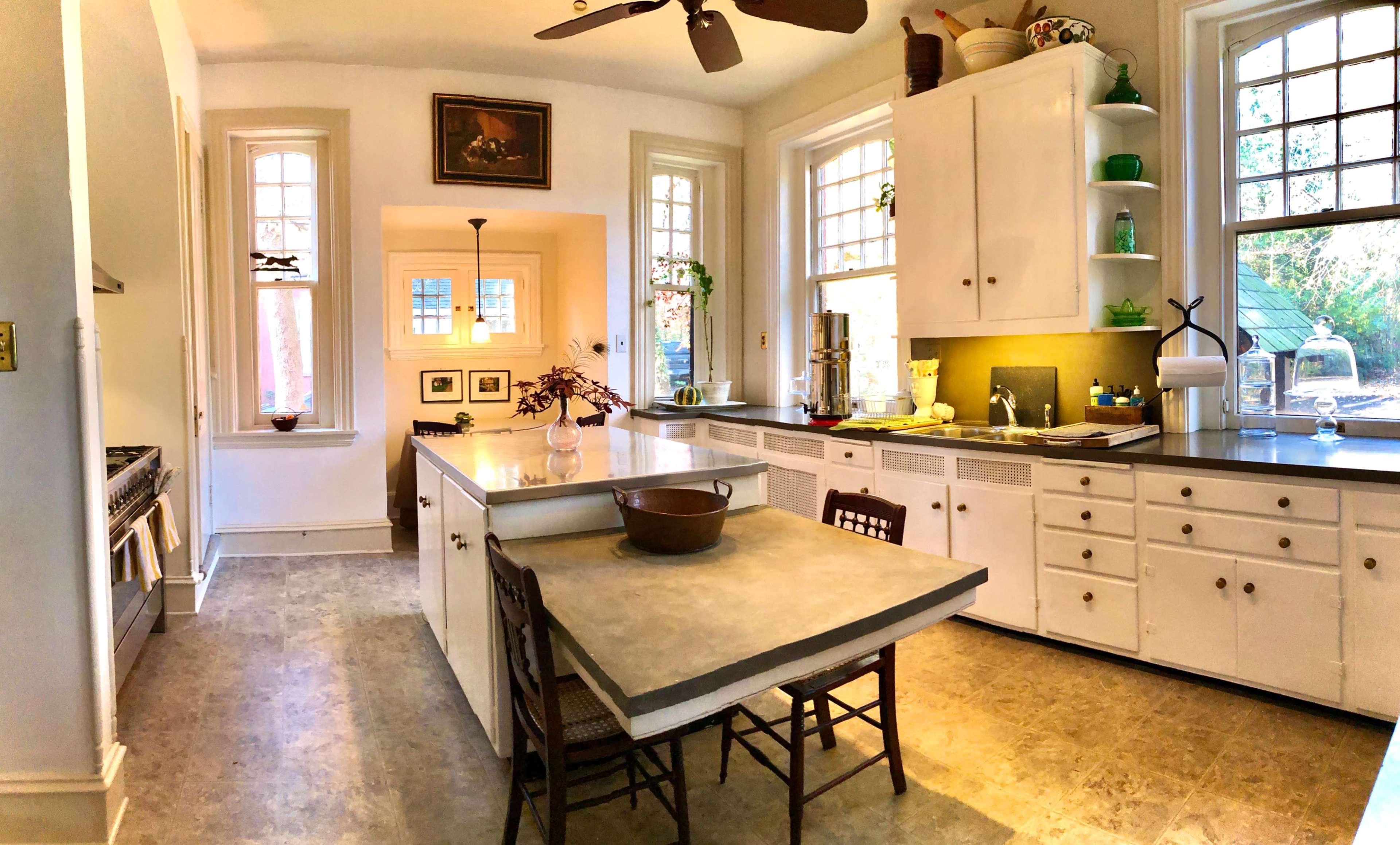A bright kitchen featuring white cabinets, a central island with a gray countertop, and various windows allowing natural light to enter.