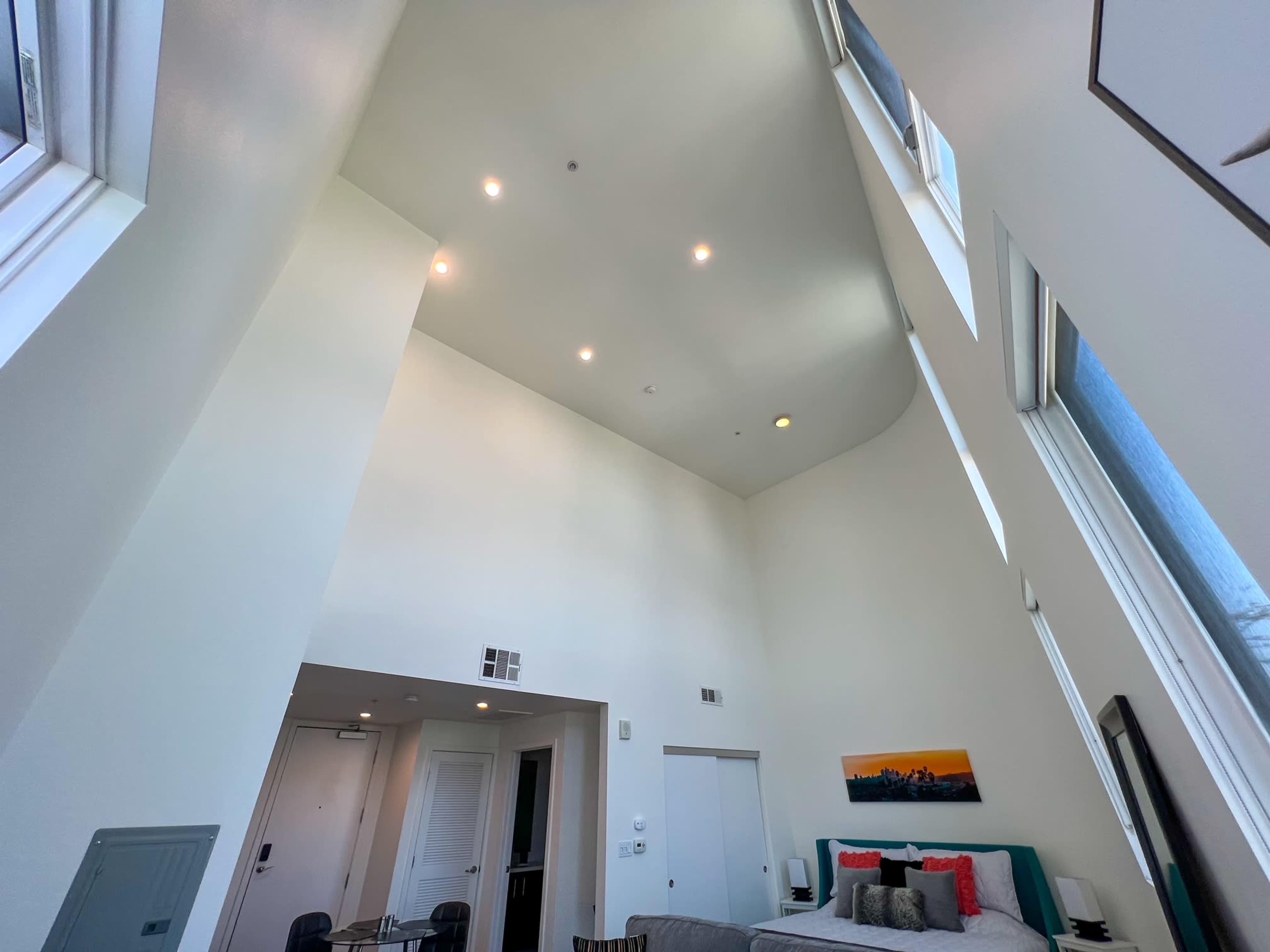 A modern room with tall, sloped white walls, large windows, and a bed positioned against one wall.