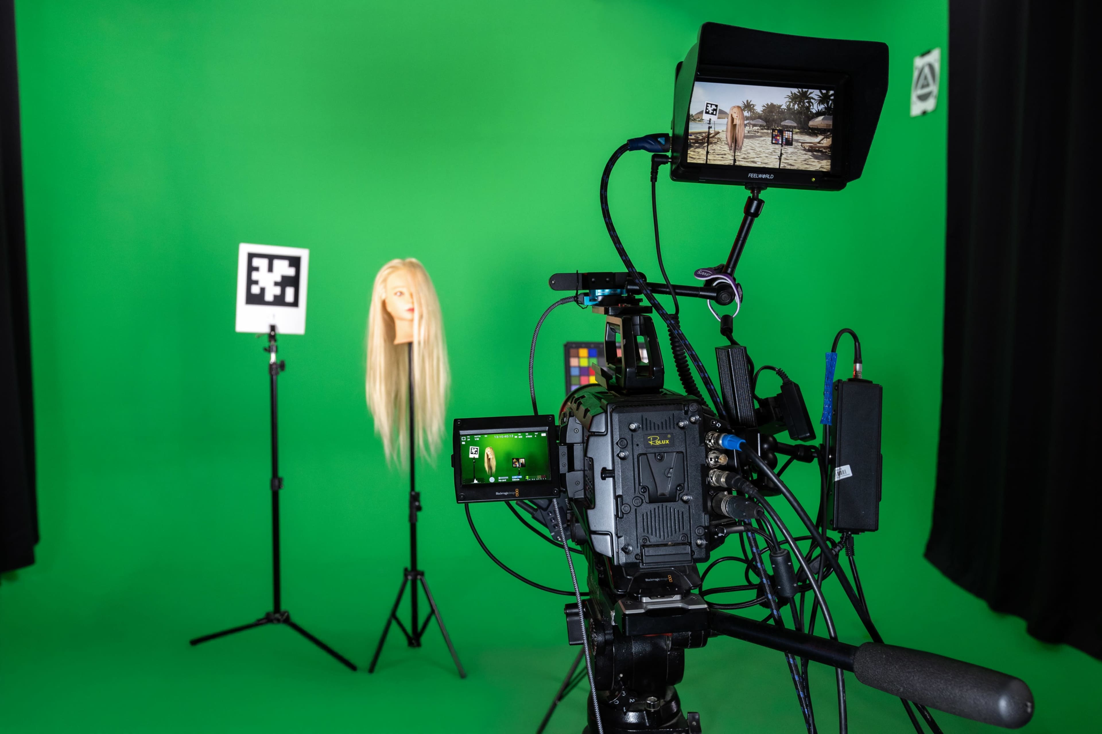 A professional camera setup focuses on a mannequin head with long hair positioned in front of a green screen.