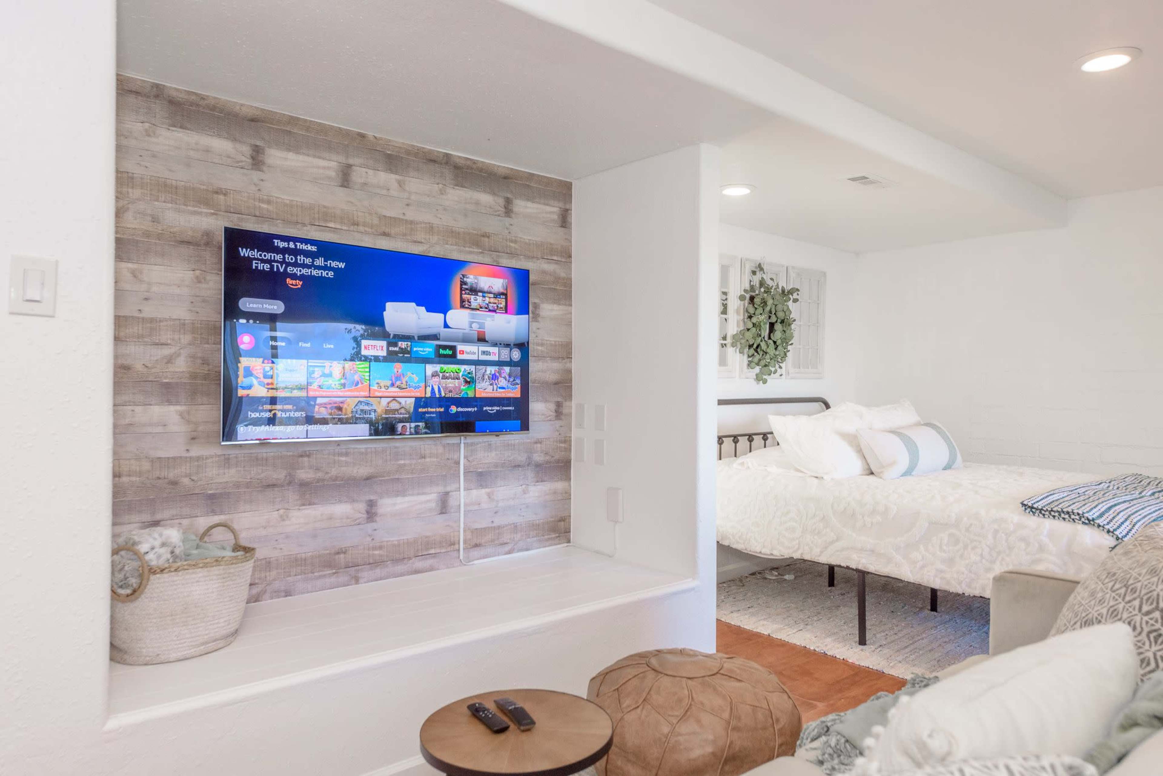 A cozy room featuring a mounted television on a wooden wall alongside a bed with light-colored bedding and a decorative rug on the floor.