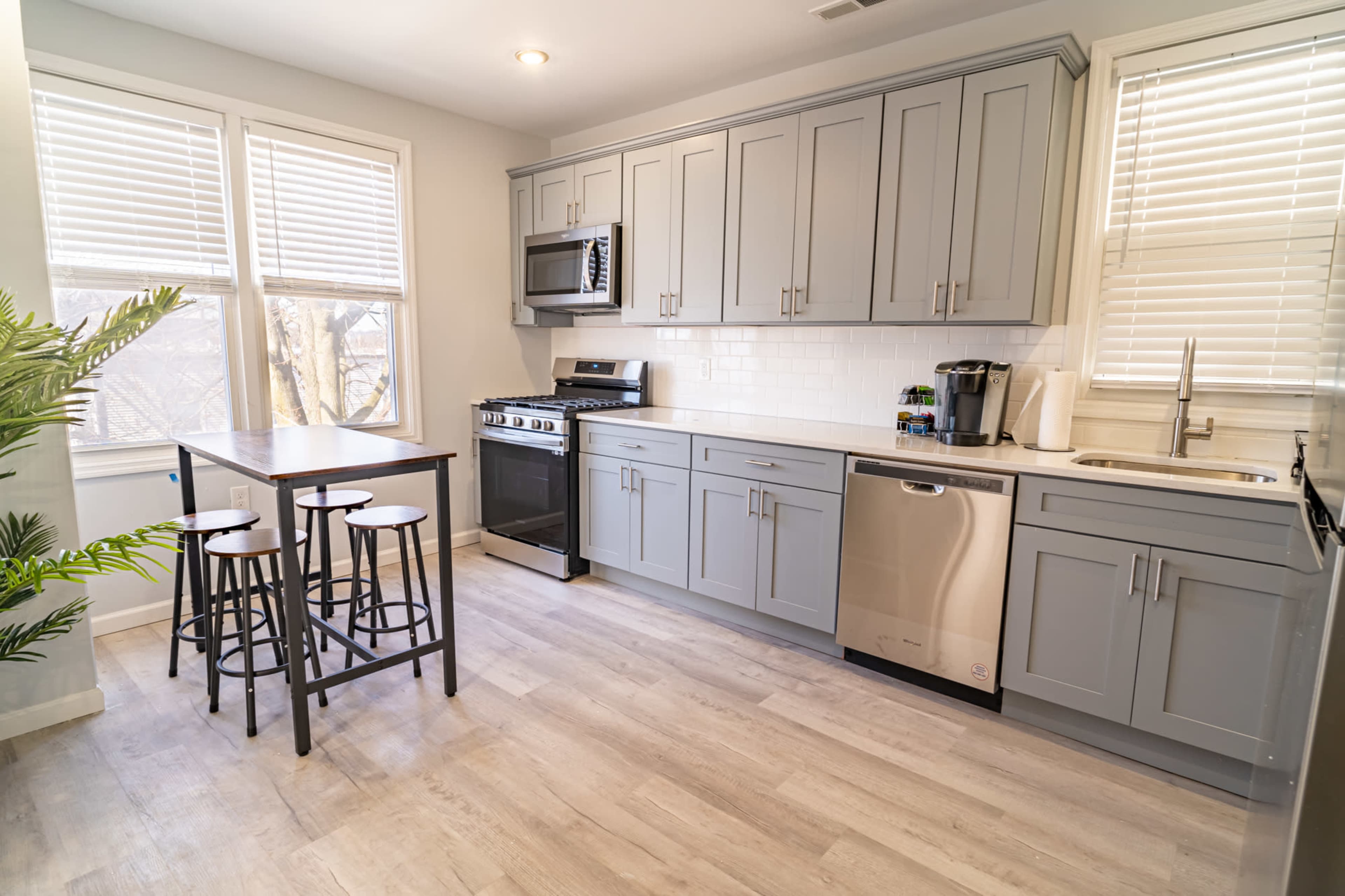 A modern kitchen with light gray cabinetry, stainless steel appliances, and a small dining table with four black stools.