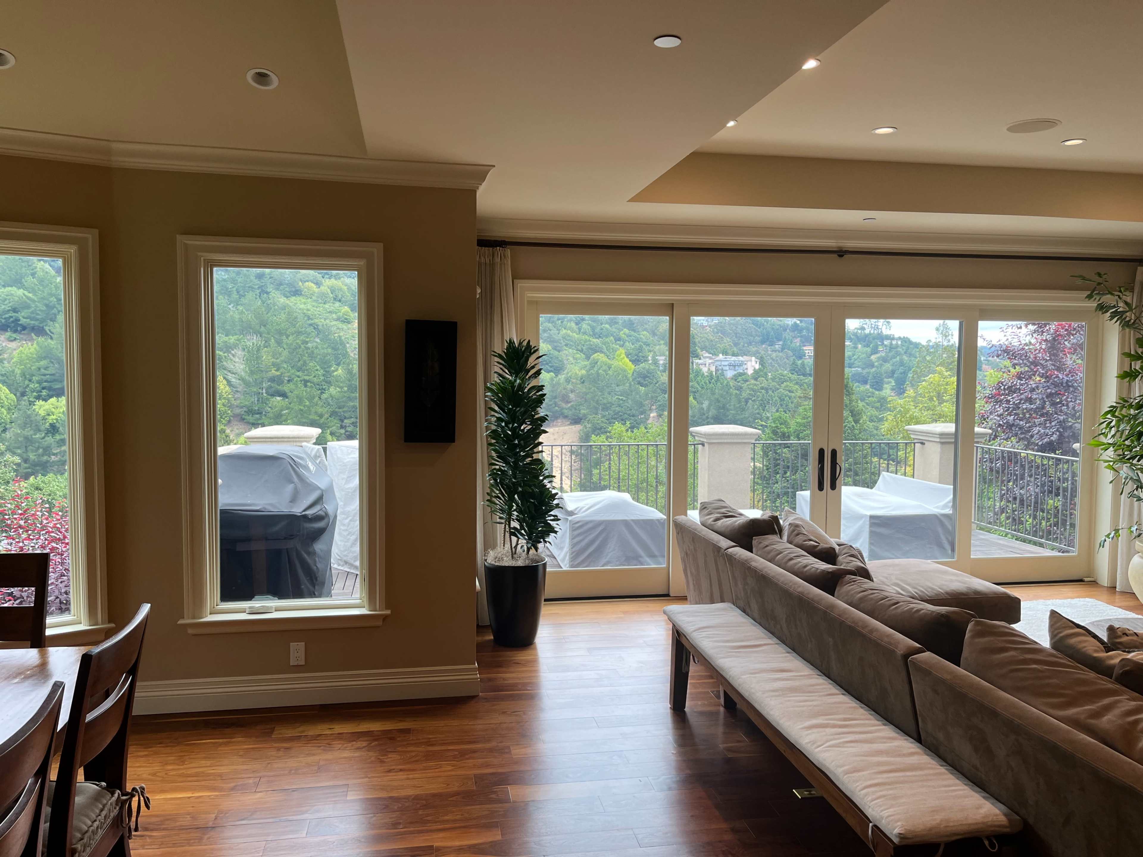 The image shows a spacious living room with a sofa and dining table, featuring large windows that overlook a forested view.