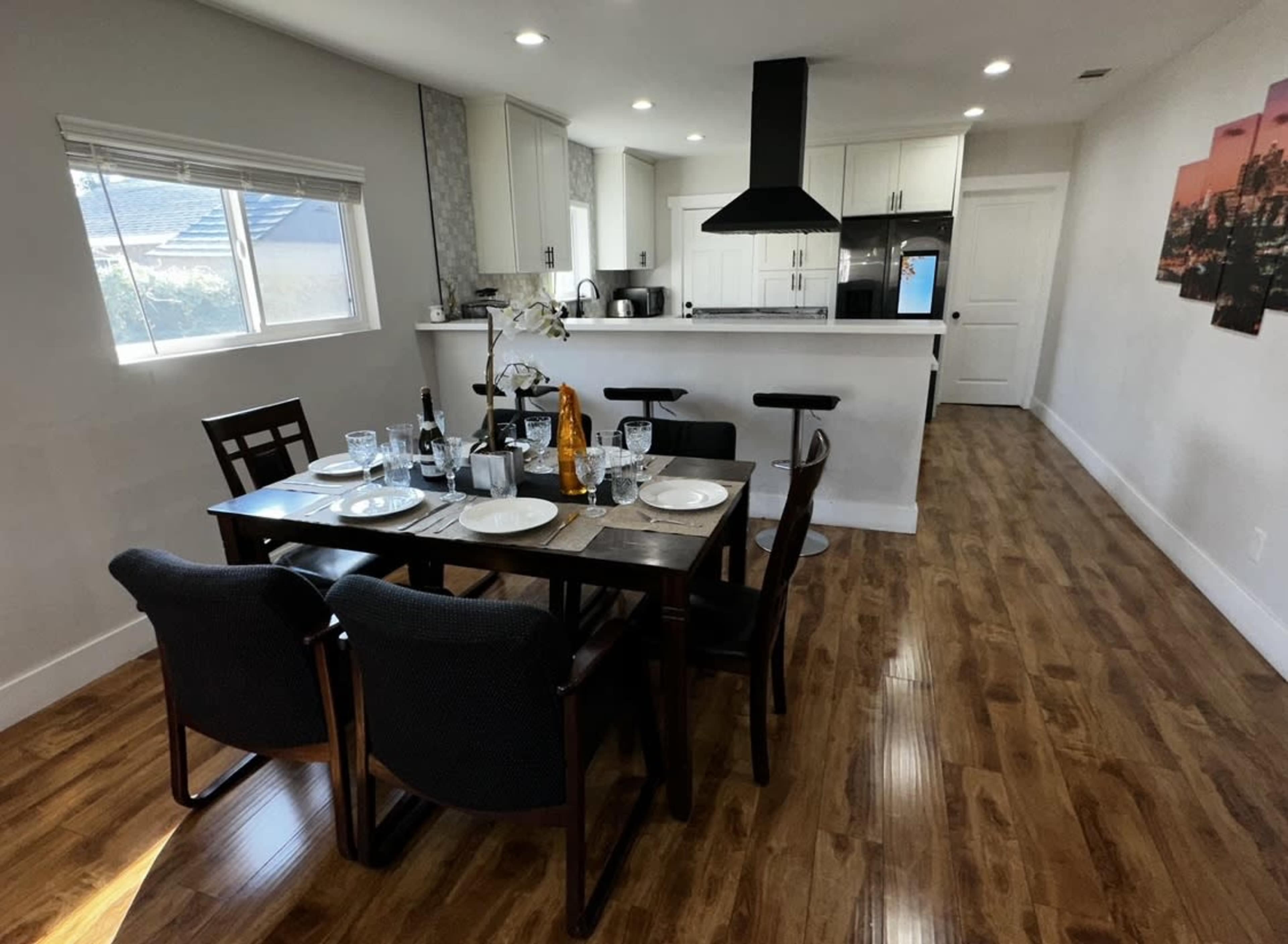 A modern dining area with a table set for a meal, surrounded by four chairs, and an open kitchen in the background.