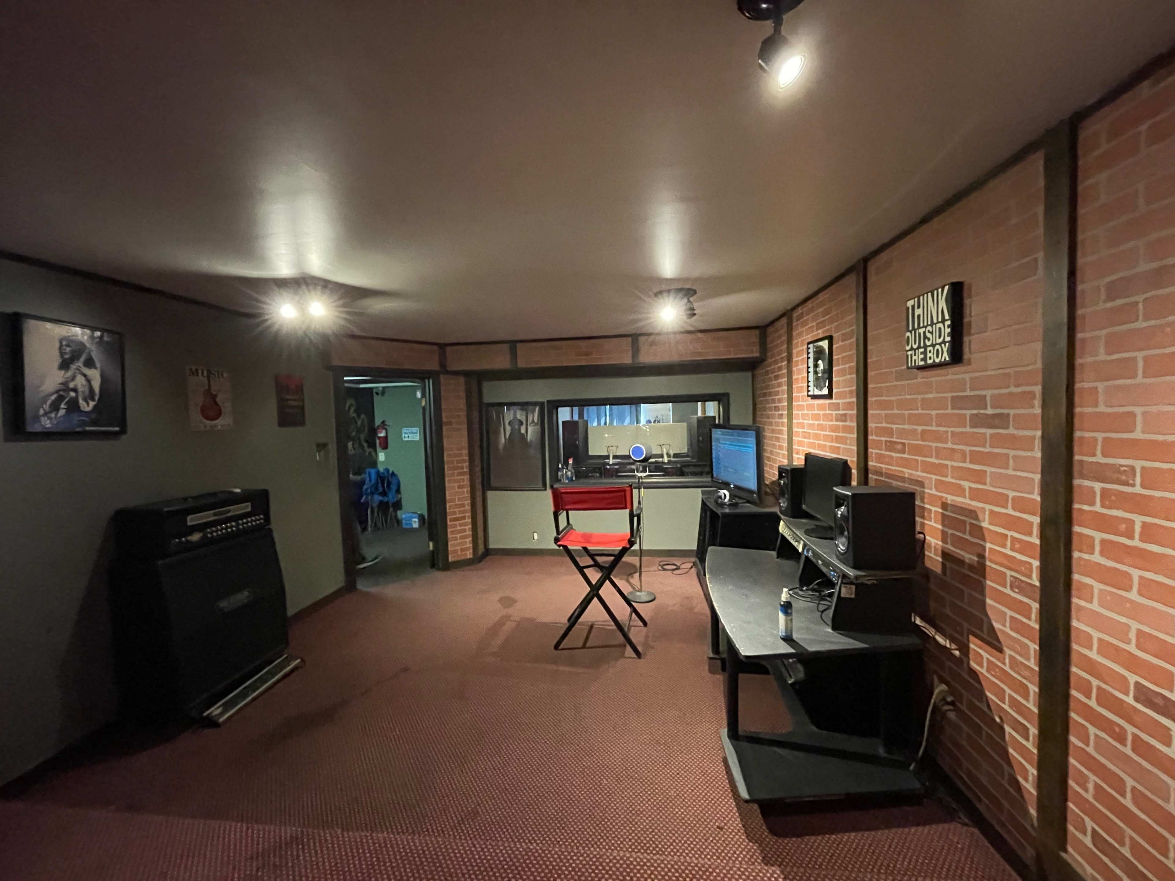 A music studio with brick walls, a black chair, a desk with a computer, and amplifiers in the corner.