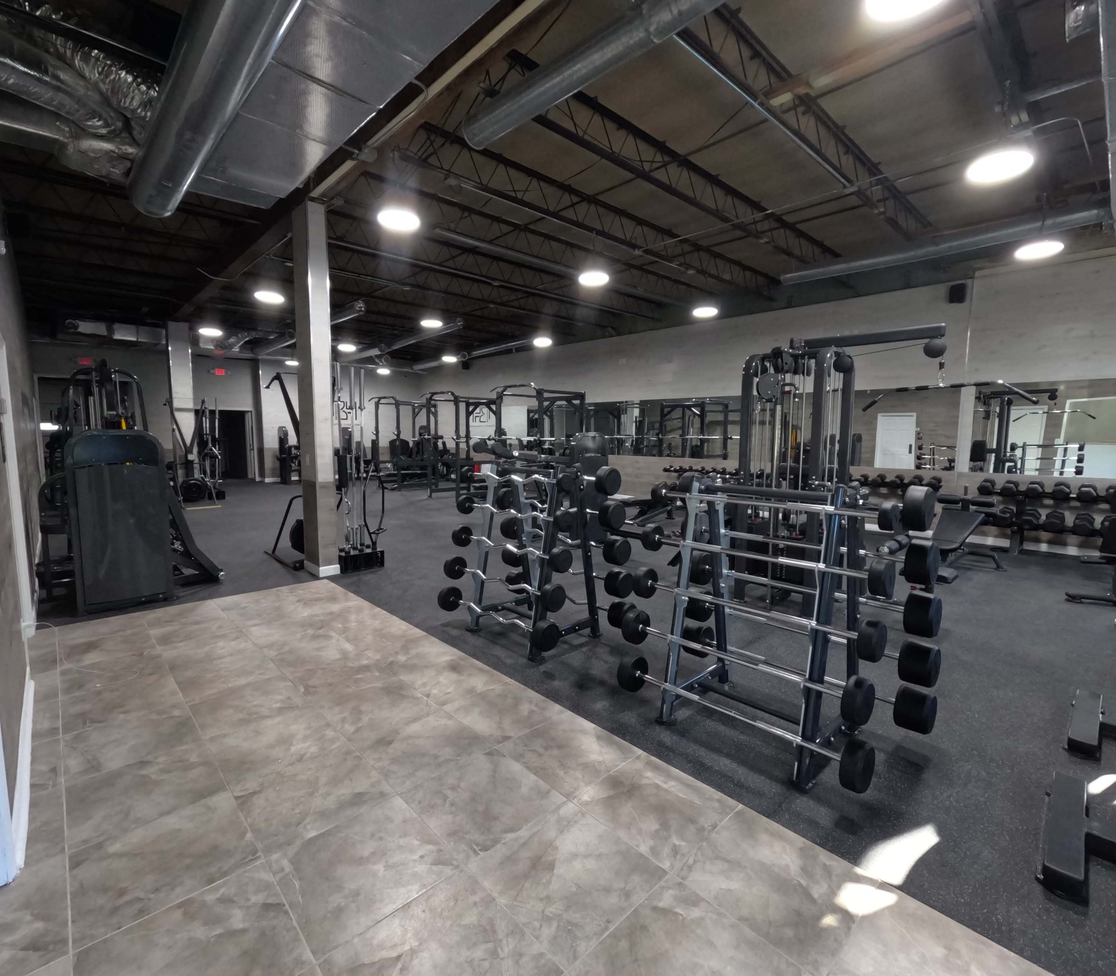 An empty gym interior with various exercise equipment, including weightlifting machines and dumbbells, arranged in an open layout.