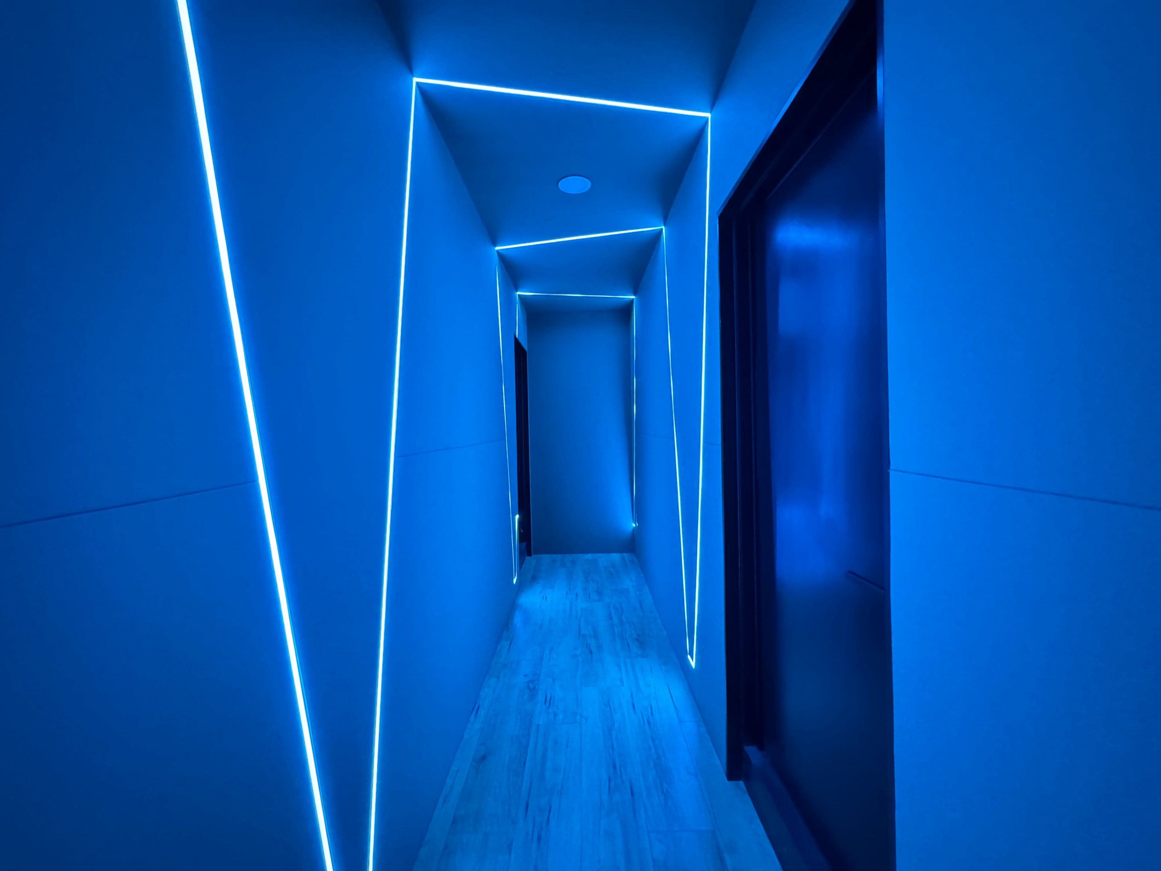 A narrow hallway features blue LED lighting that illuminates the geometric shapes formed by the walls.