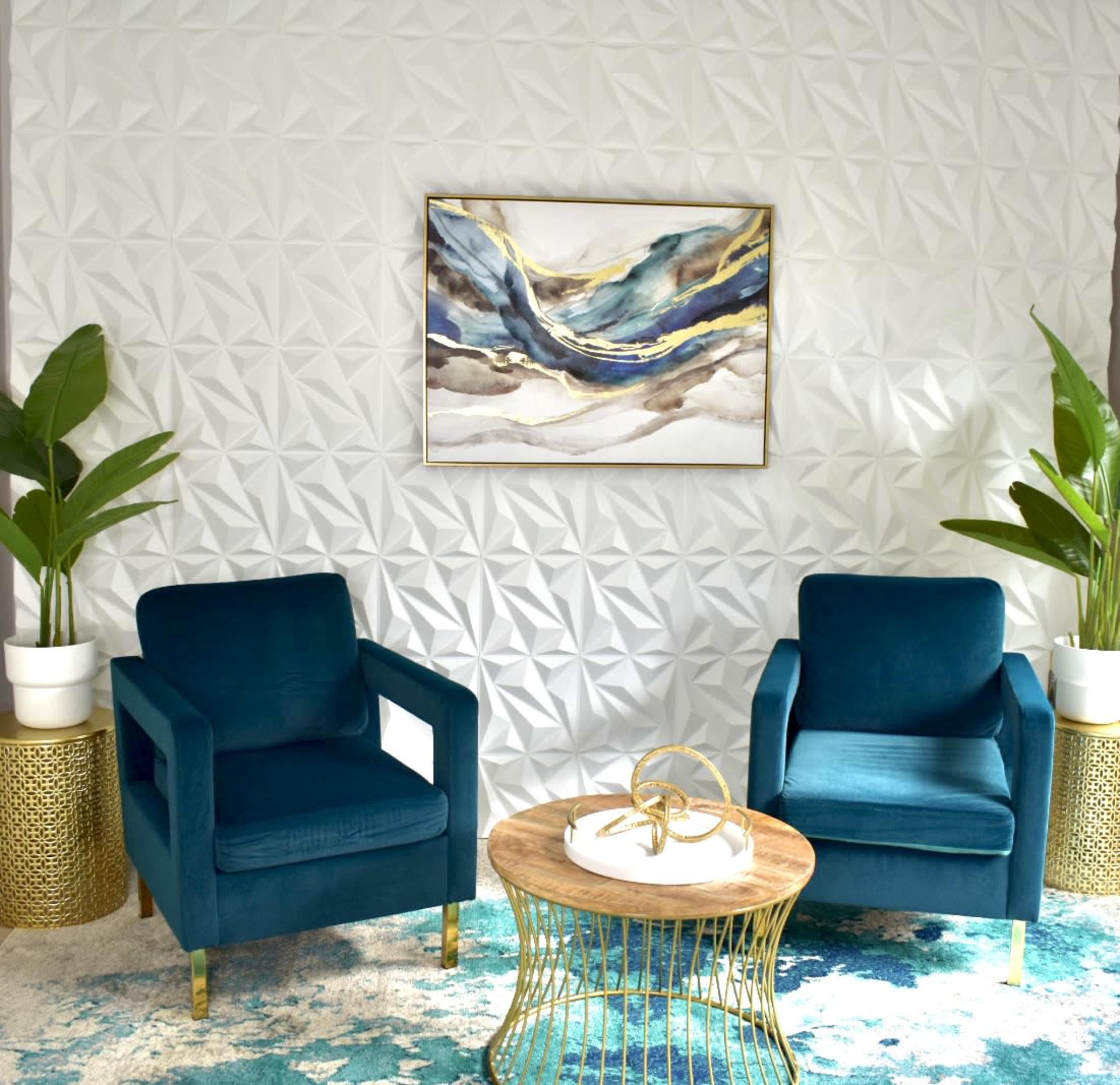 The image features two teal armchairs facing a circular wooden coffee table, set against a textured white wall with a piece of abstract art above and potted plants on either side.