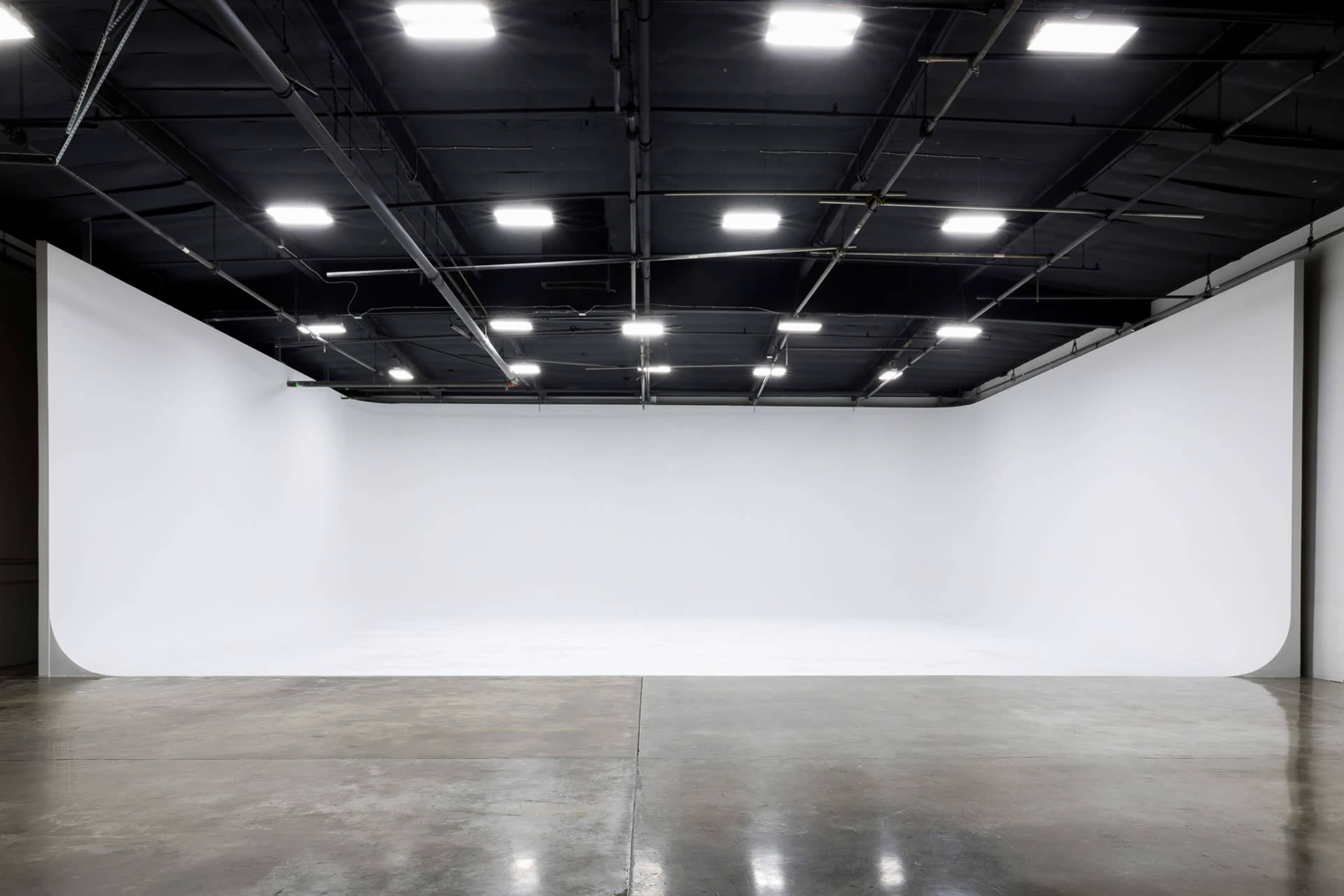 A large, empty studio space with a seamless white backdrop and overhead lighting.