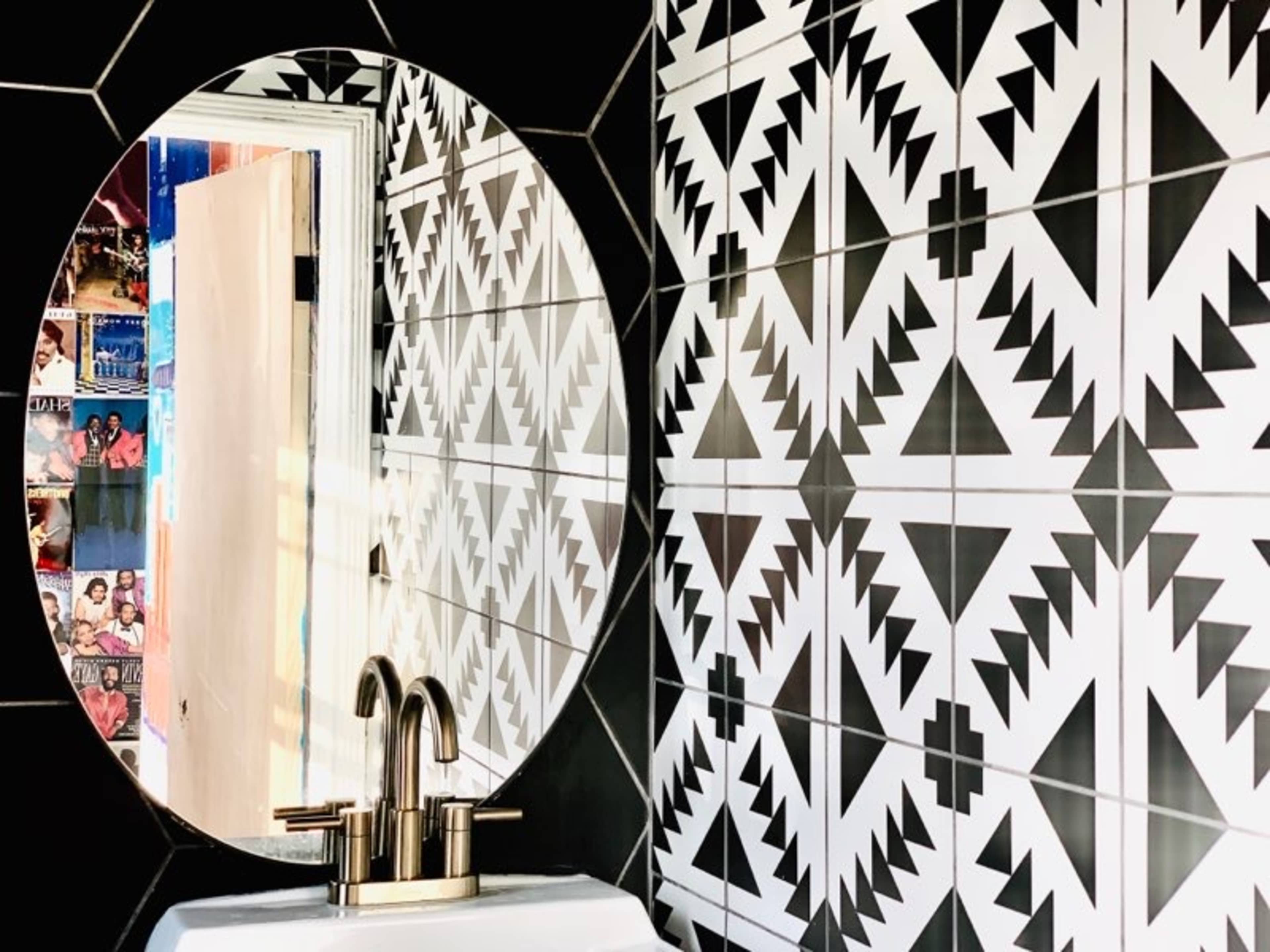 A bathroom with a round mirror reflecting geometric black and white tiles on the walls and a sink with a modern faucet.