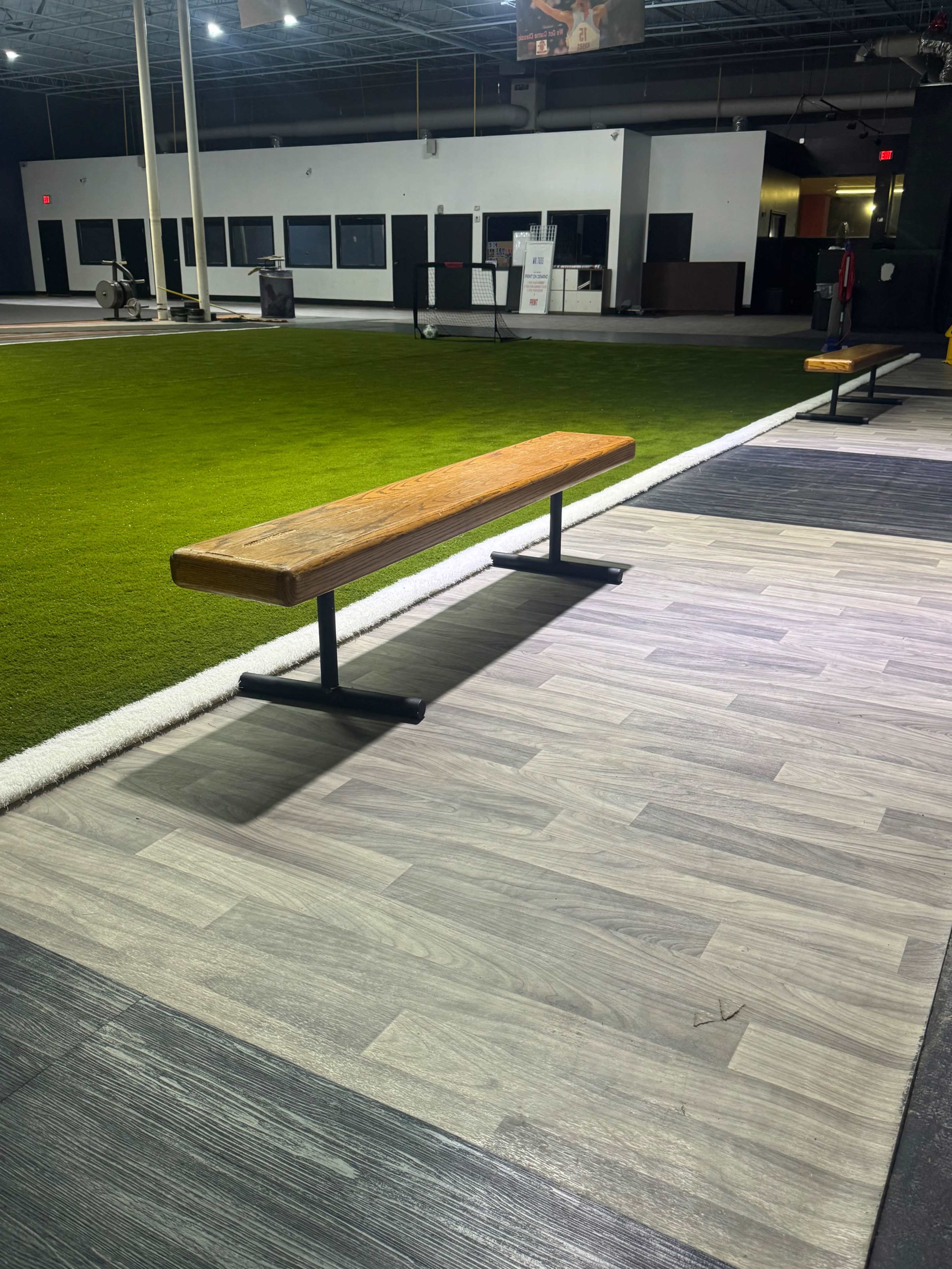 The image shows a wooden bench on a gray floor near an artificial turf area in an indoor facility.