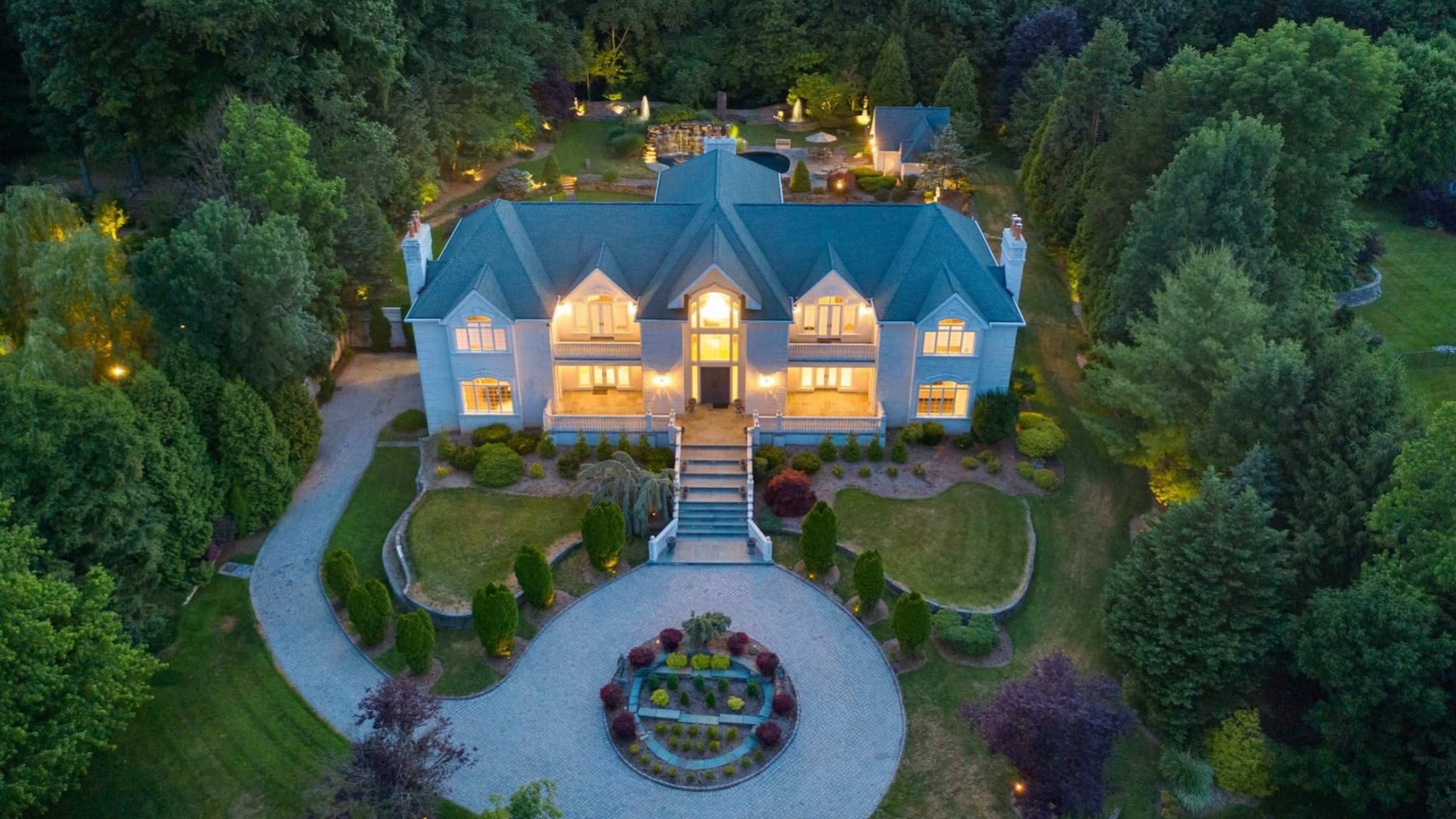 A large, elegant mansion with a green roof is surrounded by well-manicured gardens and a circular driveway.