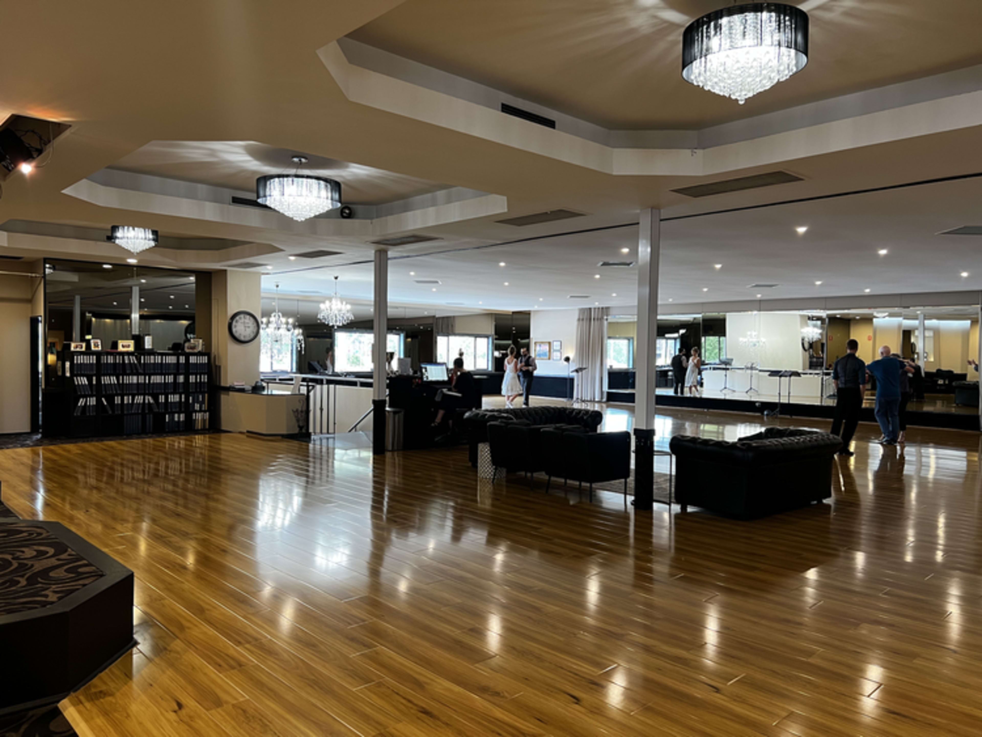 The spacious interior features a polished wooden floor, modern chandeliers, and seating areas with dark furnishings.