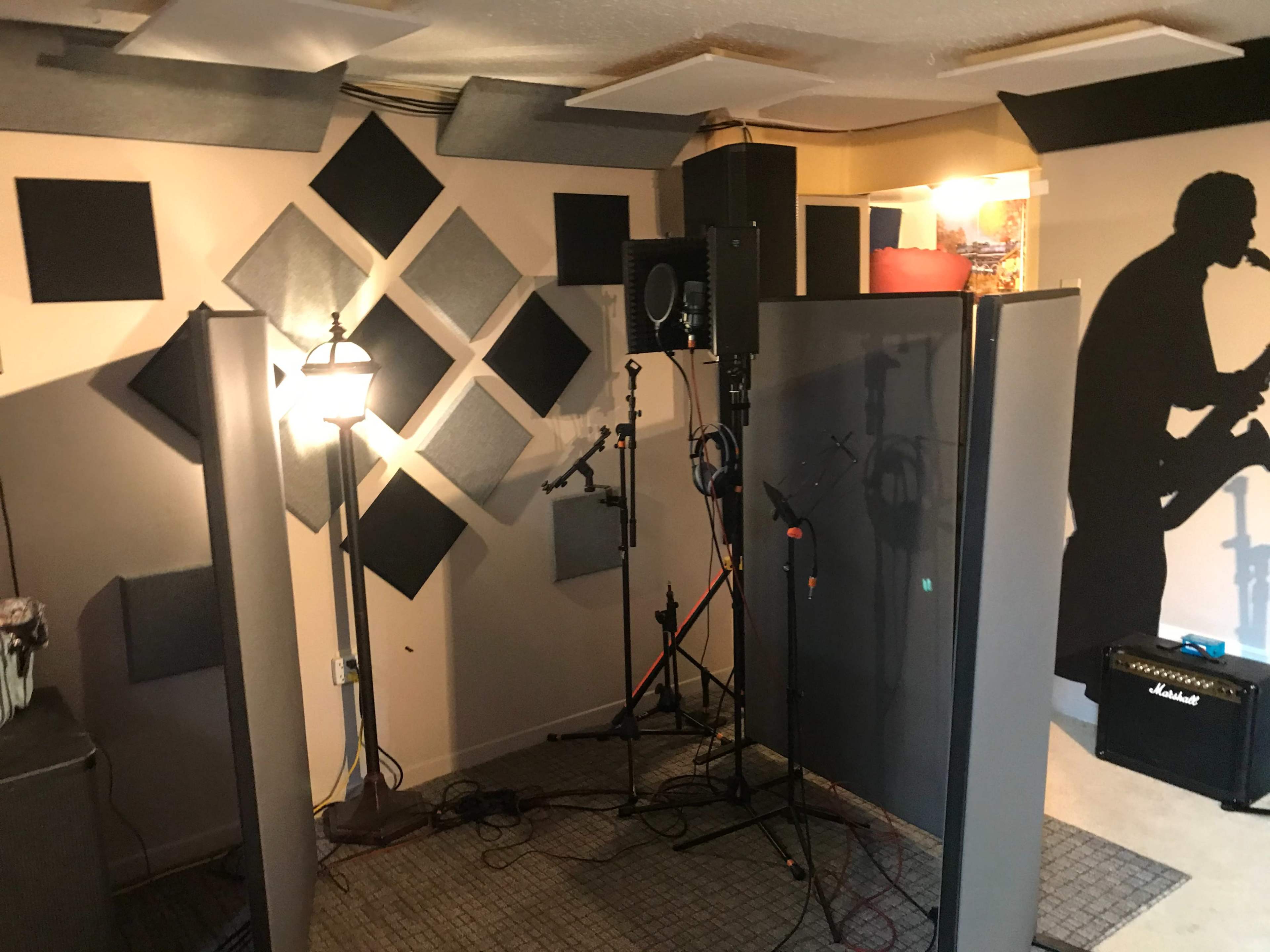 The image shows a soundproof recording studio with acoustic panels on the walls and a microphone setup, including a guitar amplifier in the corner.