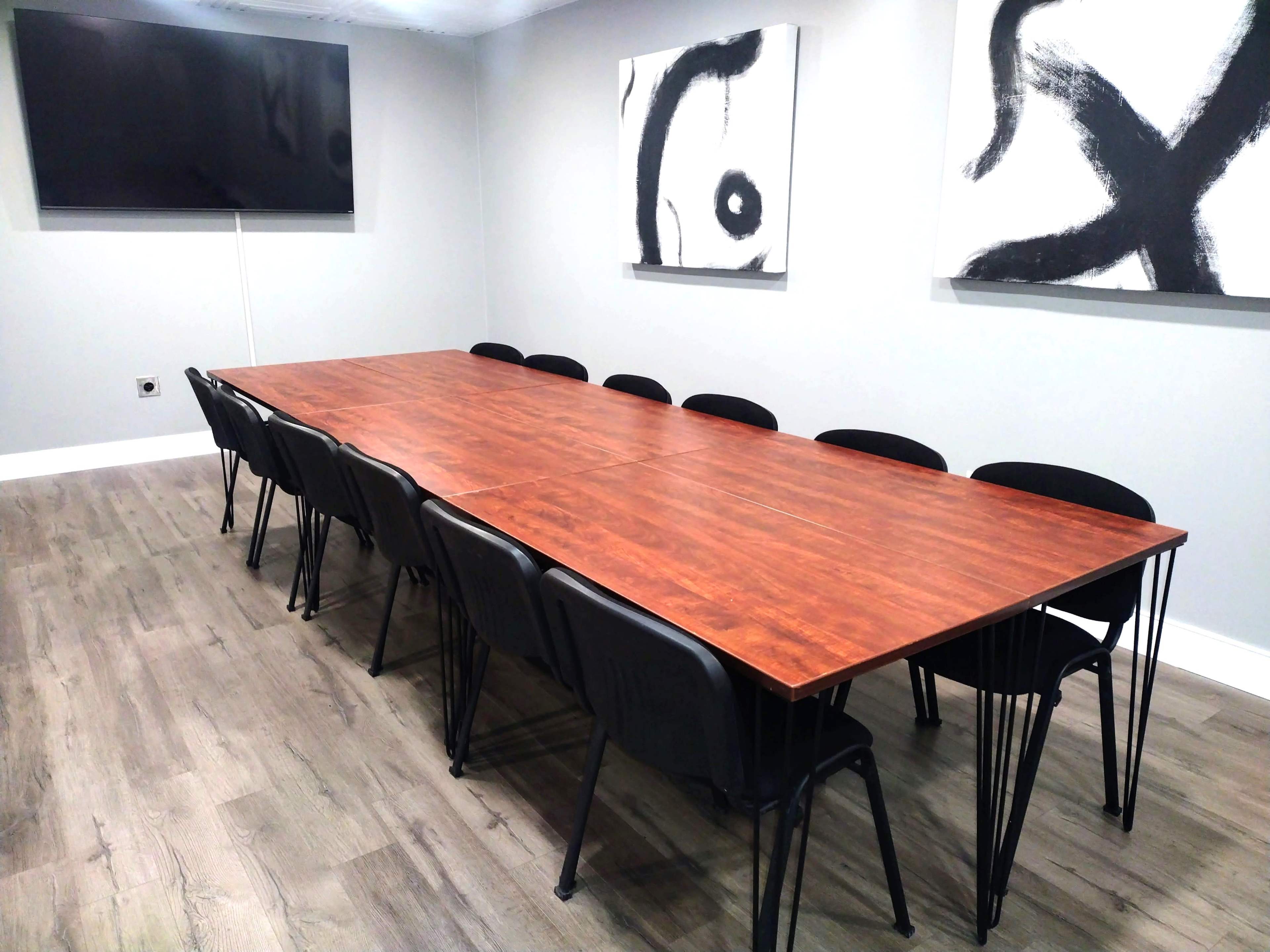 A conference room with a long wooden table surrounded by black chairs, and two abstract paintings on the walls.