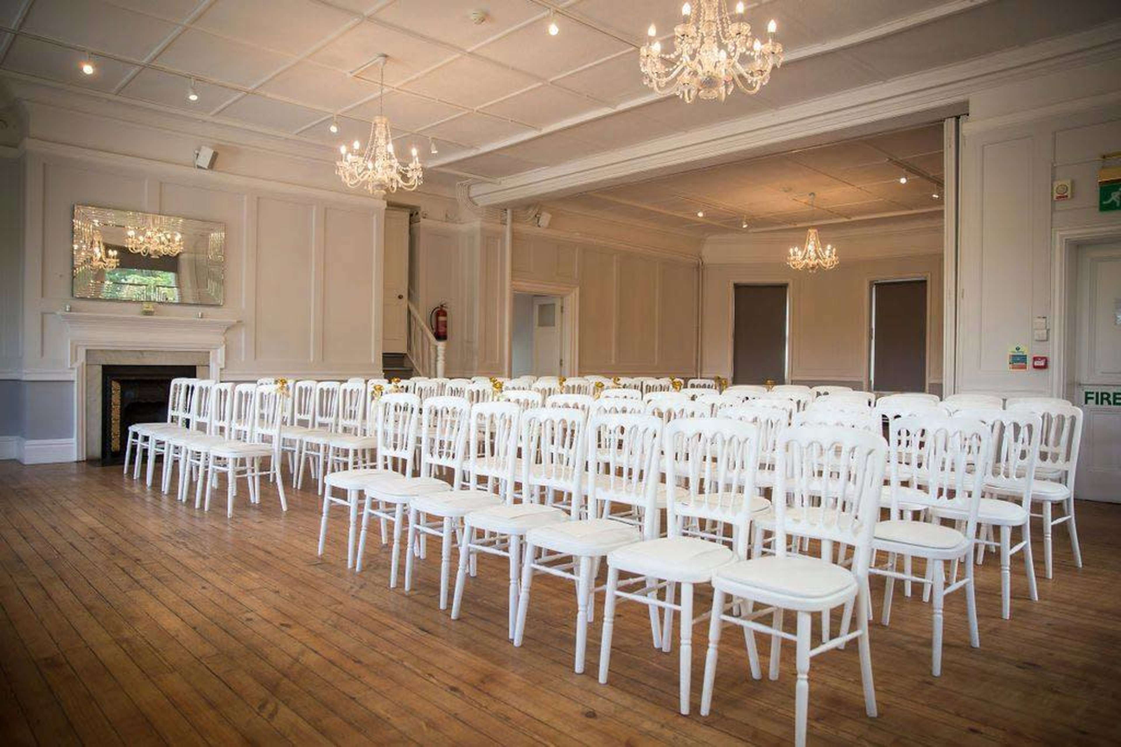 A spacious room with white chairs arranged in neat rows on a wooden floor, illuminated by chandeliers.