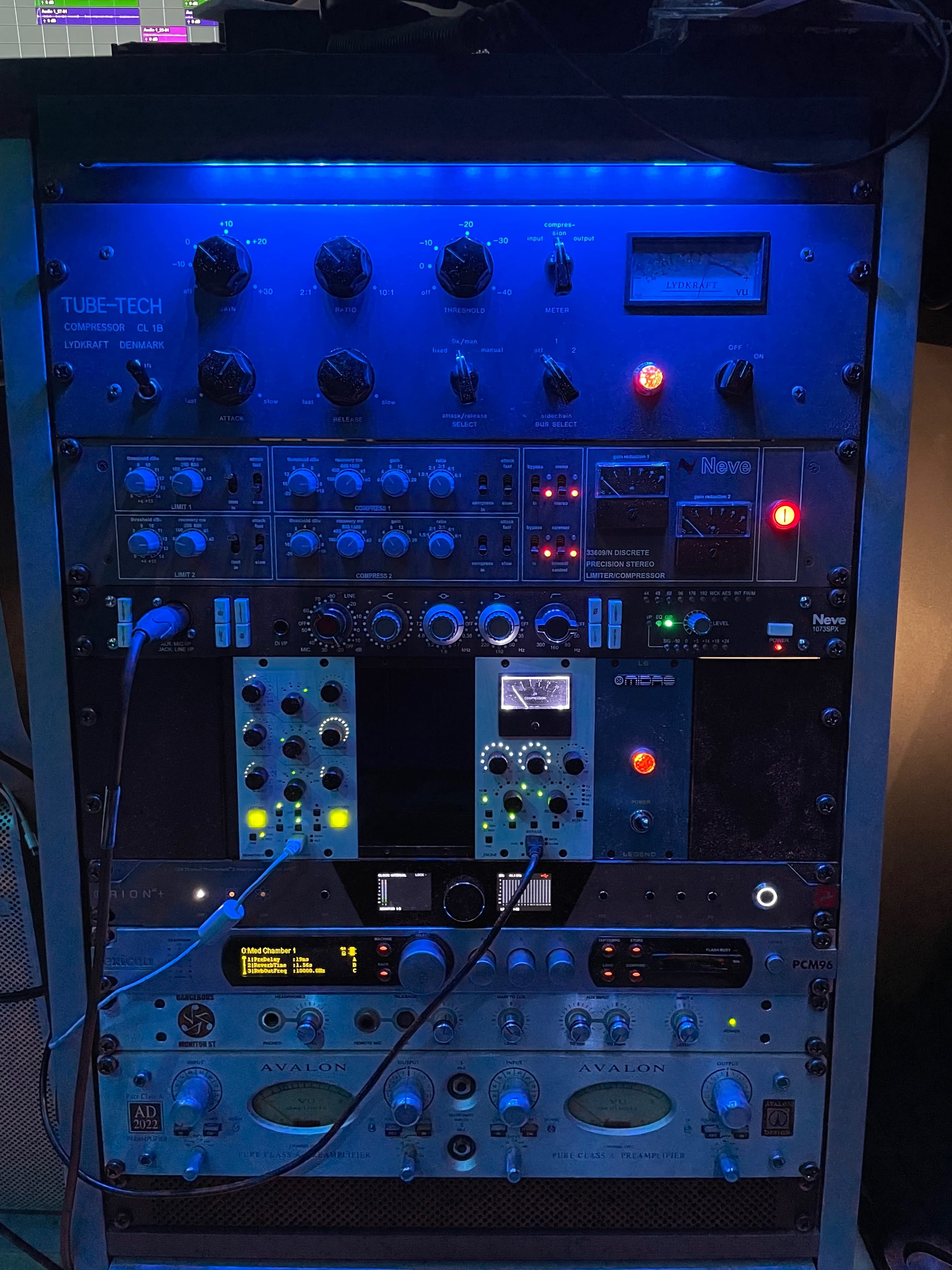 A rack of audio equipment featuring various knobs, meters, and illuminated displays, organized into multiple sections.