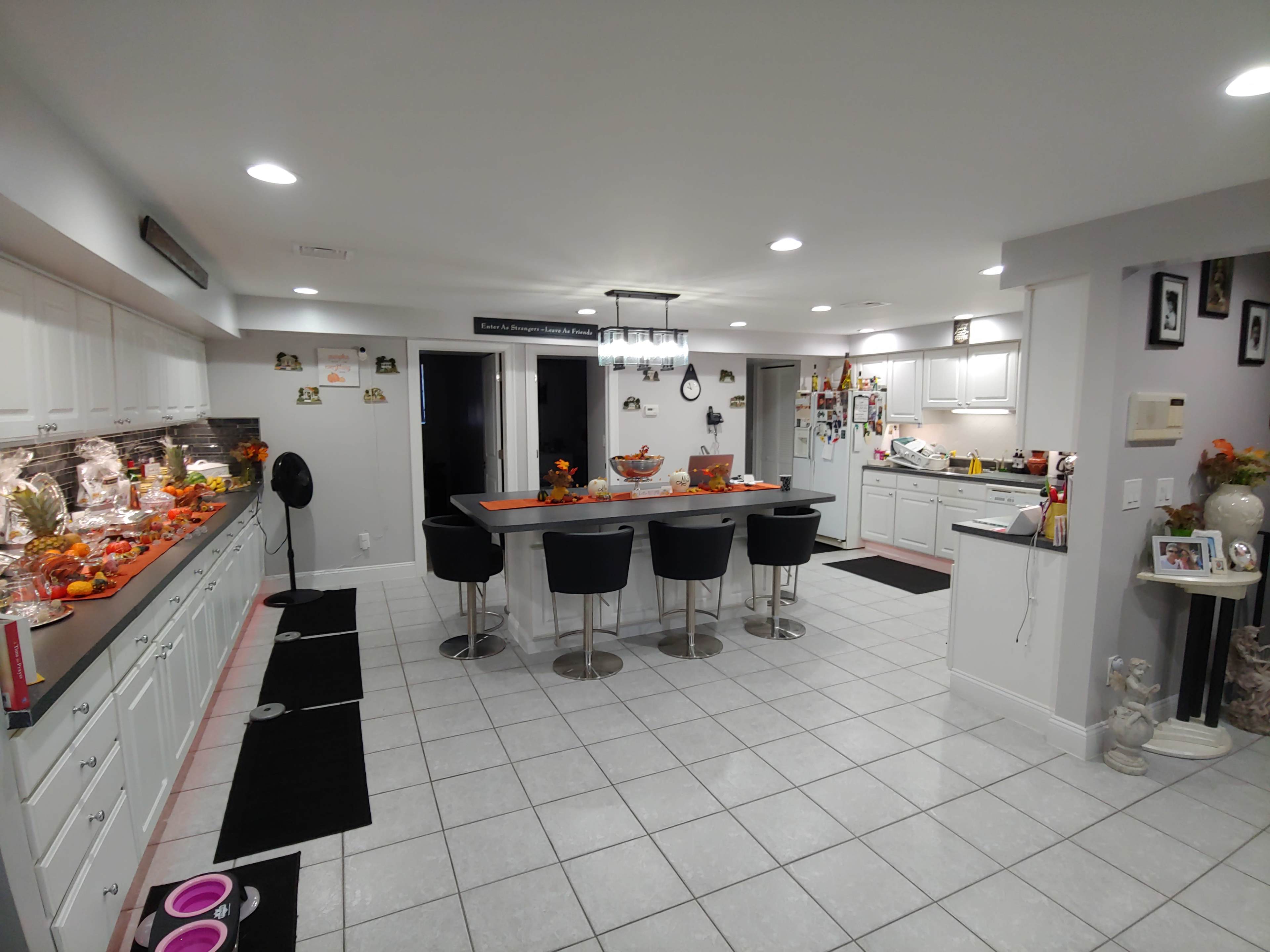 A spacious kitchen features white cabinets, a central island with bar stools, and autumn decorations on the countertops.