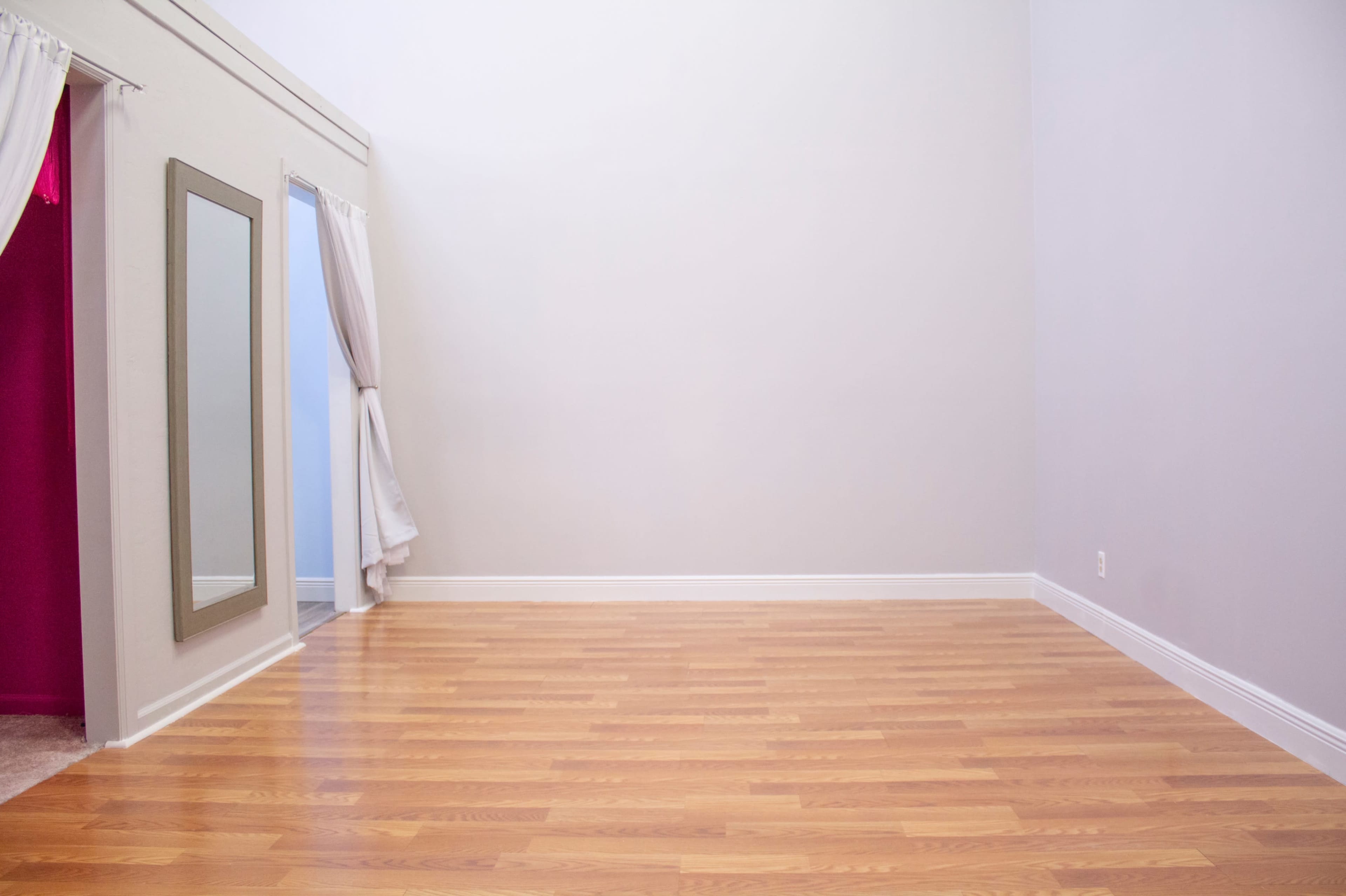 A spacious room with light wooden flooring, a large mirror, and a pink curtain on one side.