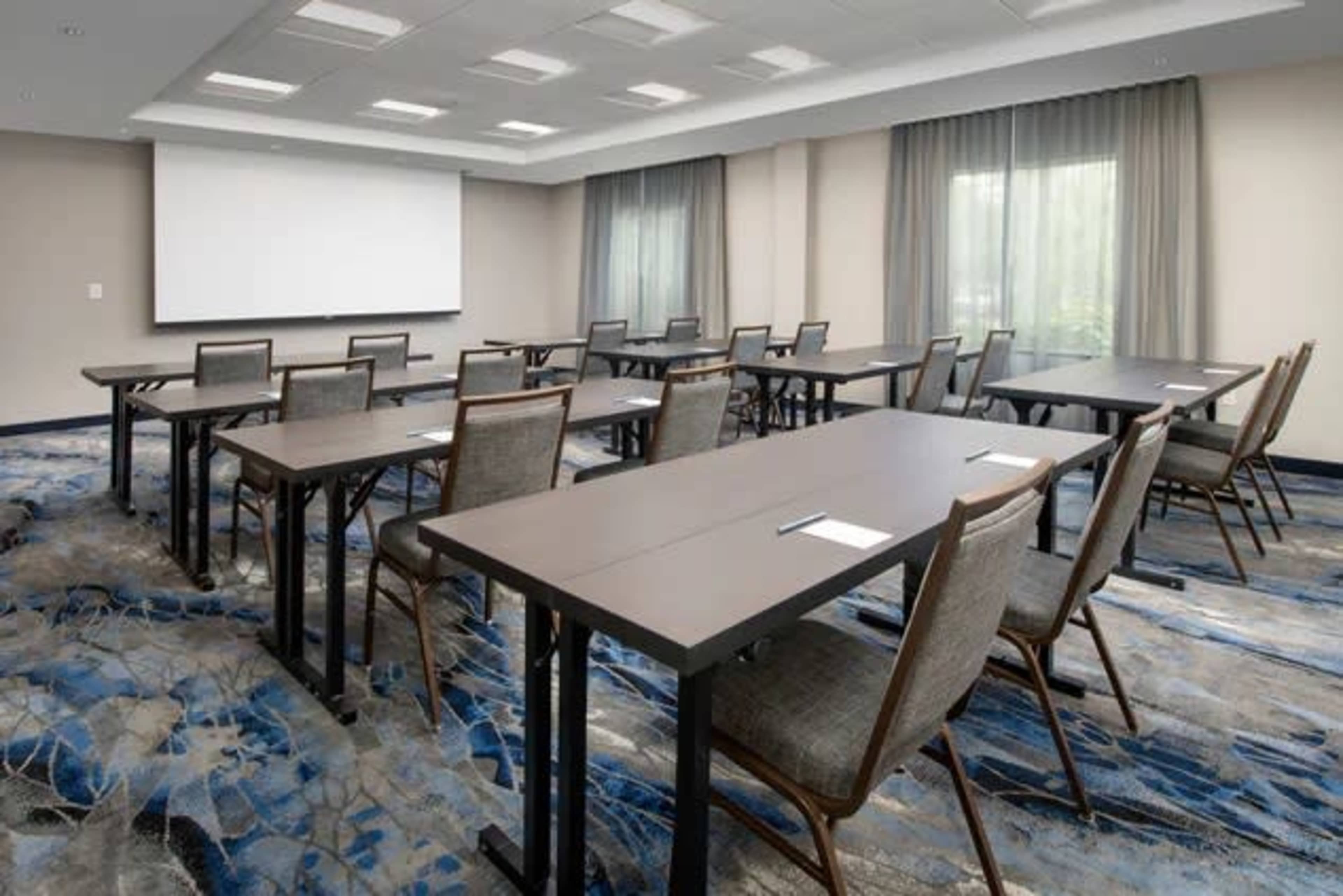 The image shows a conference room set up with rows of tables and chairs facing a blank projection screen.