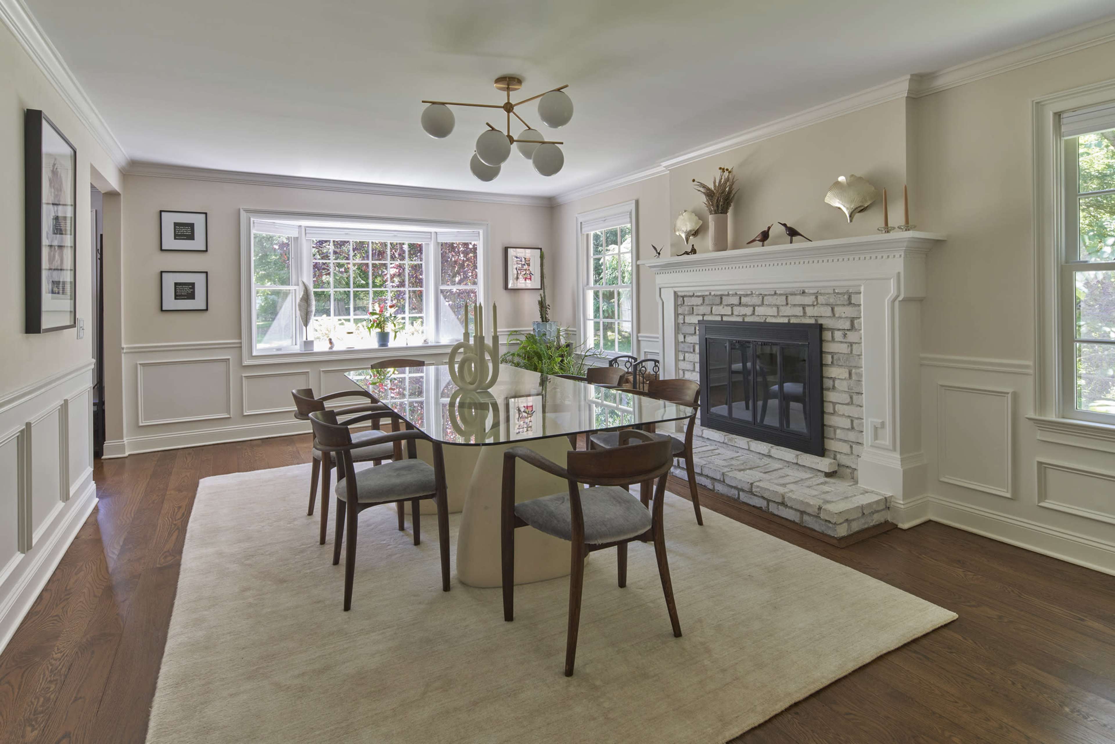 A modern dining area features a glass table surrounded by wooden chairs, with a stone fireplace and large windows letting in natural light.