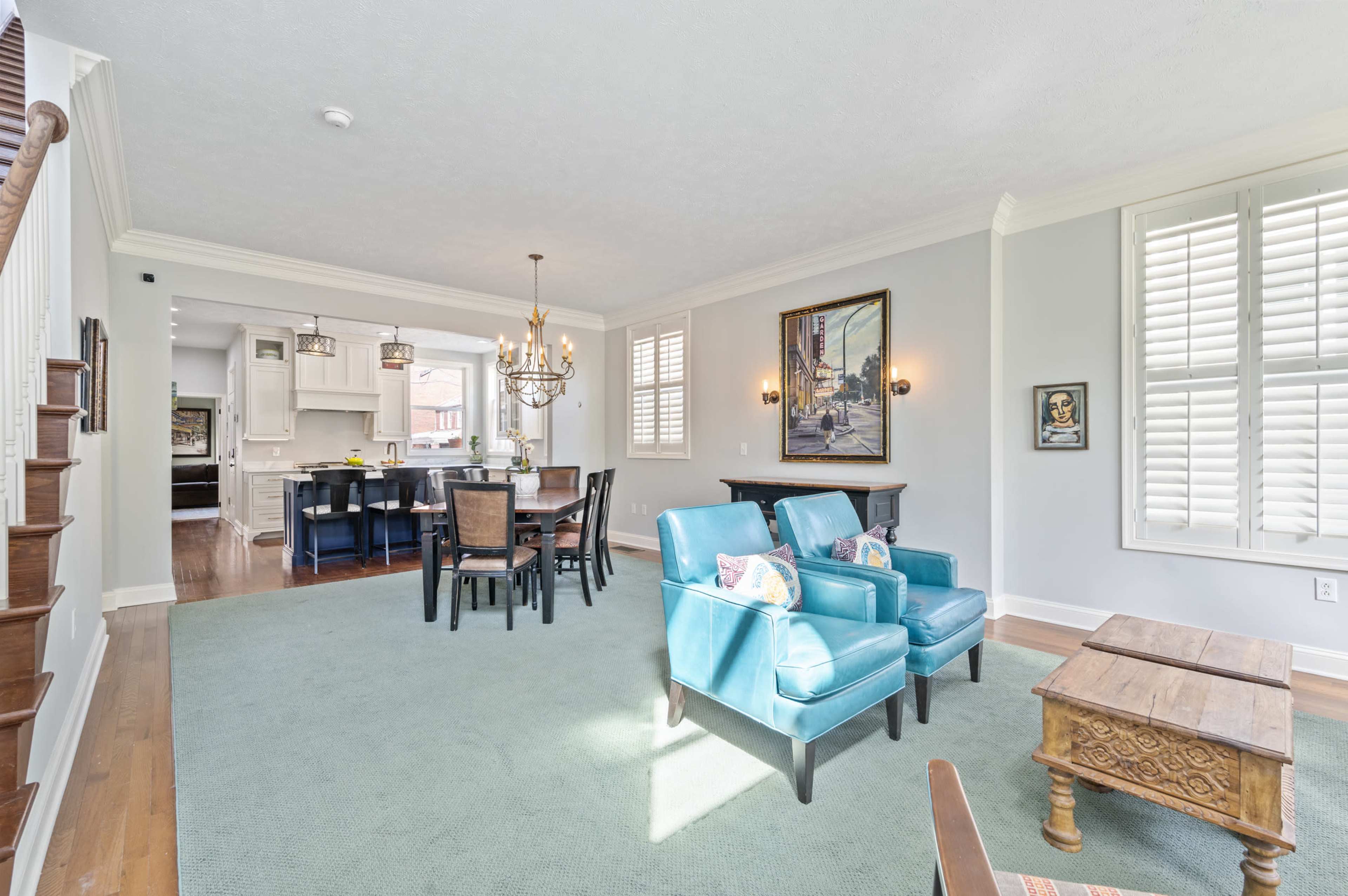 A bright living space with teal chairs and a wooden coffee table, leading into a dining area and kitchen.
